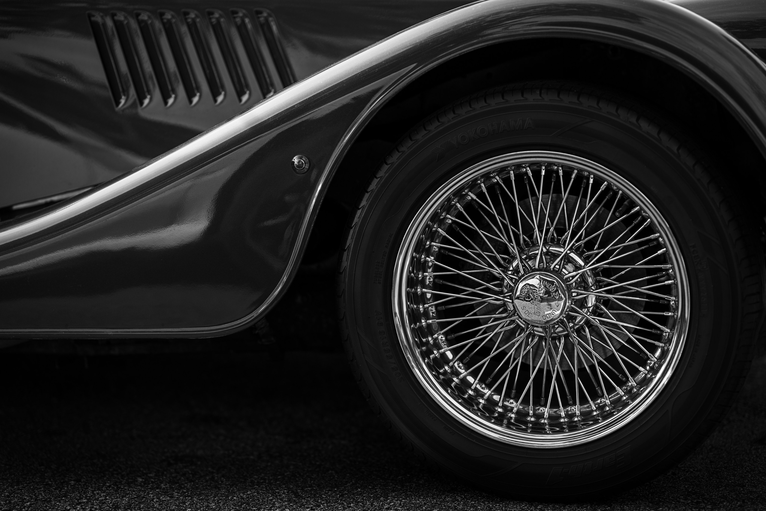 Jaguar wire-spoke wheel detail – elegant black-and-white macro of a classic Jaguar wire wheel and sweeping fender, perfect for luxury automobile marketing and editorial storytelling.
