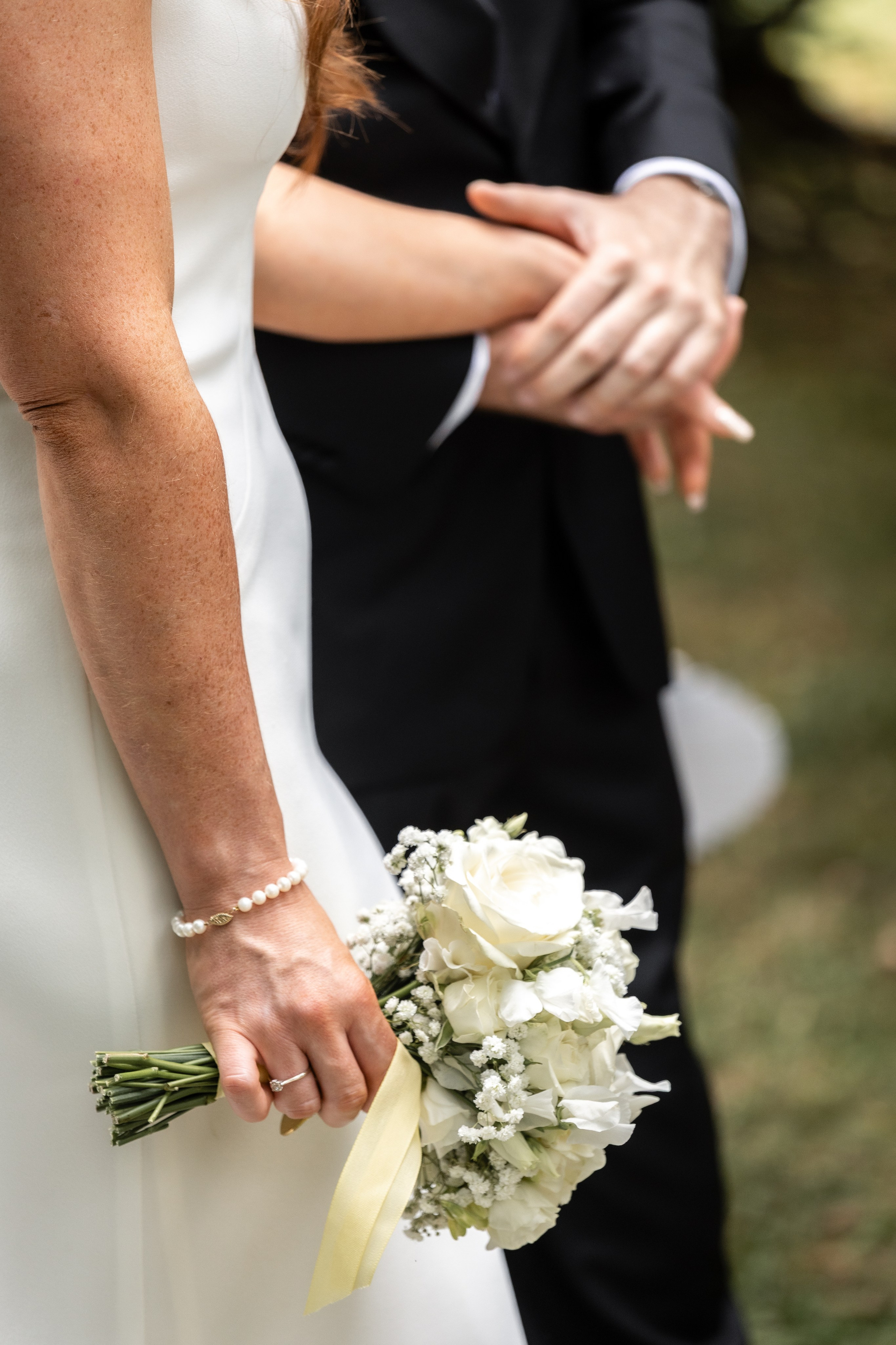 Groom's hand holding the bride's hand beside her white bouquet