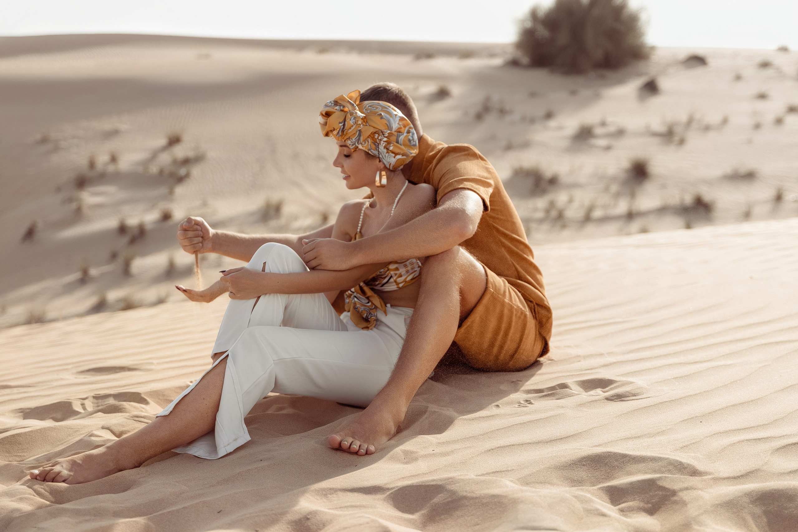 A couple enjoying a playful moment in the desert, laughing and embracing each other with golden sand dunes stretching behind them. Dubai, United Arab Emirates