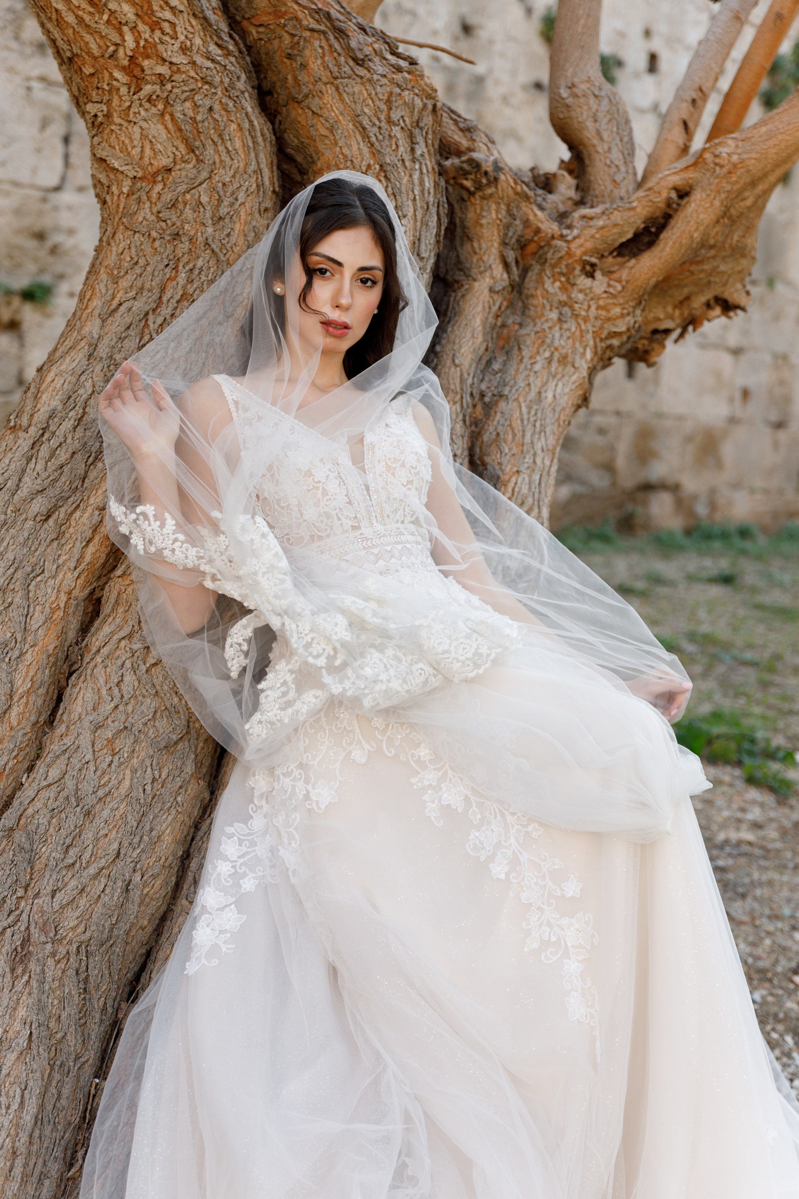 A stunning bride gazes thoughtfully in the enchanting alleys of Rhodes' Old Town, her flowing wedding dress complementing the rustic charm of the cobblestone streets and ancient architecture. The editorial-style portrait captures her poise and the romantic atmosphere of the medieval surroundings, bathed in warm, golden light.
