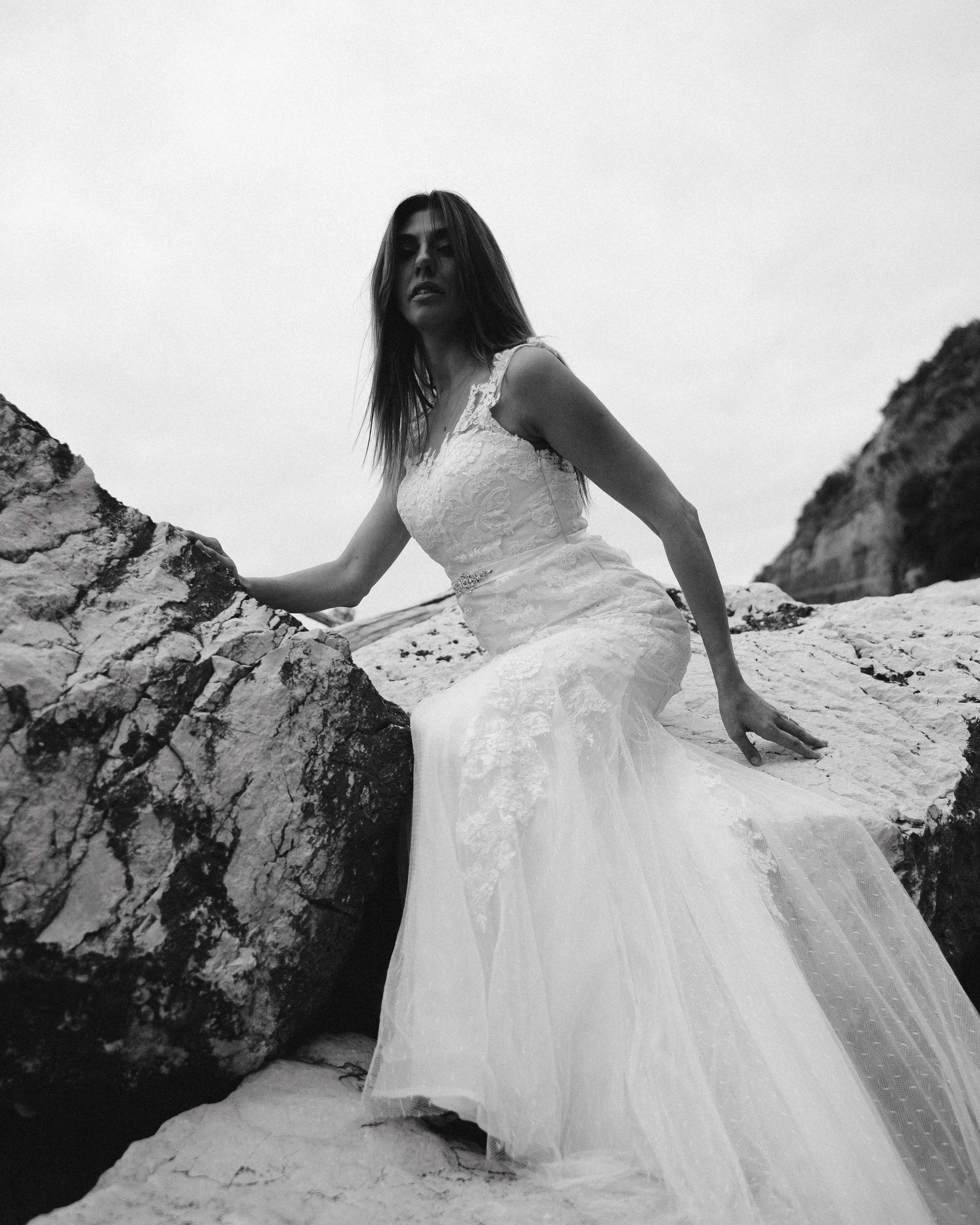 Black and white portrait of a bride posing frontally on rocky seaside cliffs