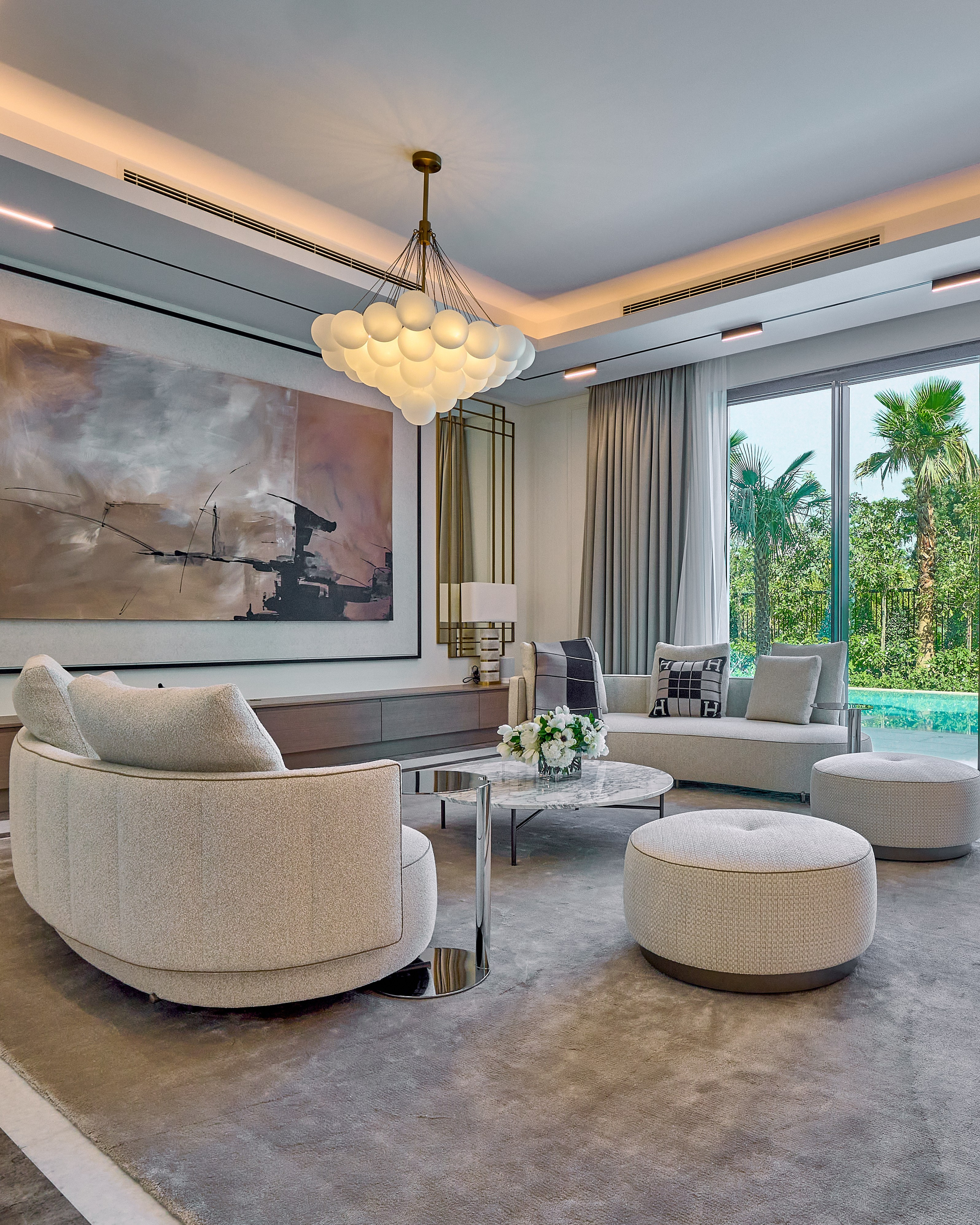 Elegant living room with circular sofas and lush greenery outside the window in Al Barari villa, Dubai.