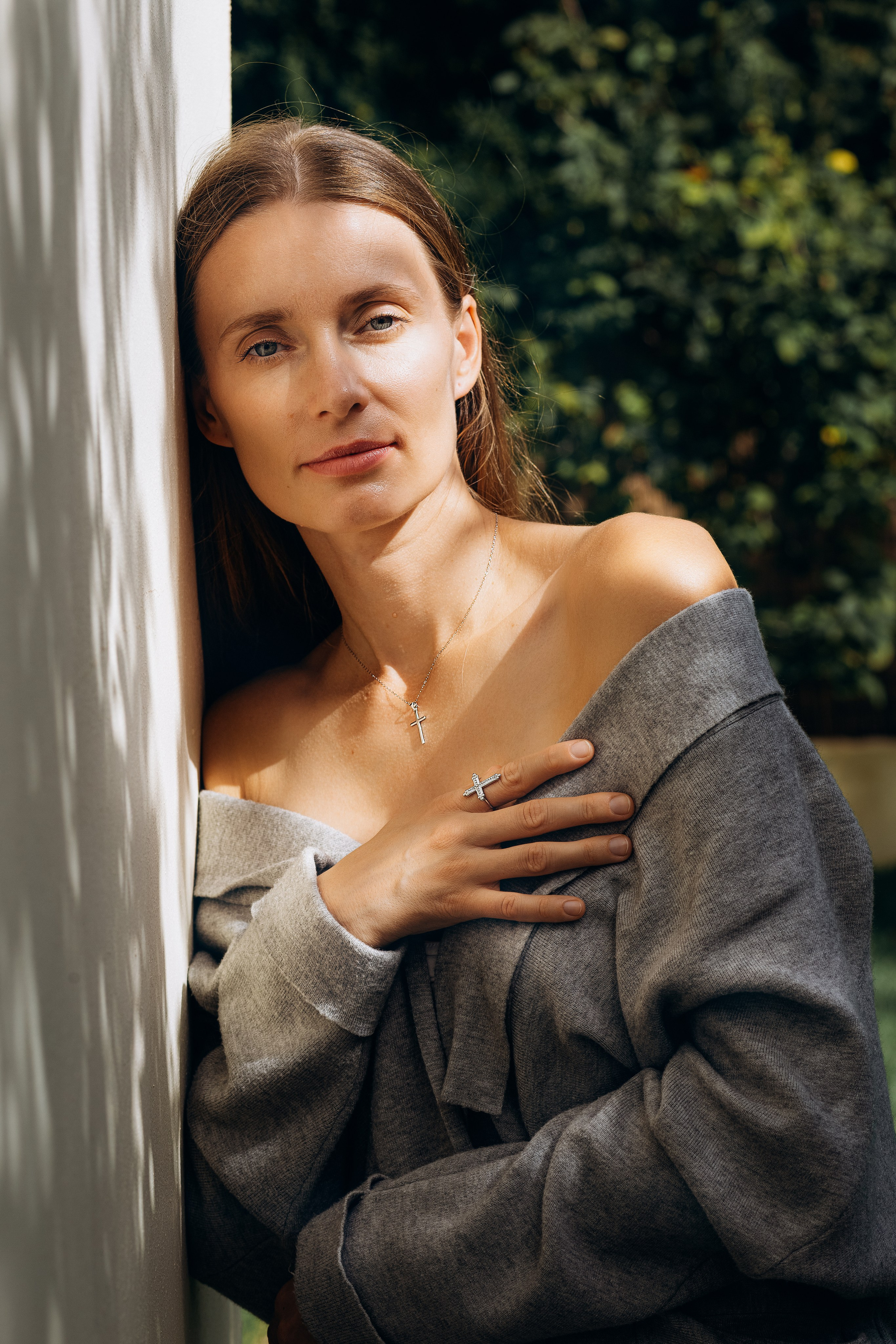Elegant brand portrait of a woman leaning by a sunlit wall, showcasing delicate jewelry and relaxed fashion styling. Captured in Valencia, Spain, this image is ideal for brand, product, or content photoshoots highlighting natural beauty and lifestyle aesthetics in Spain.