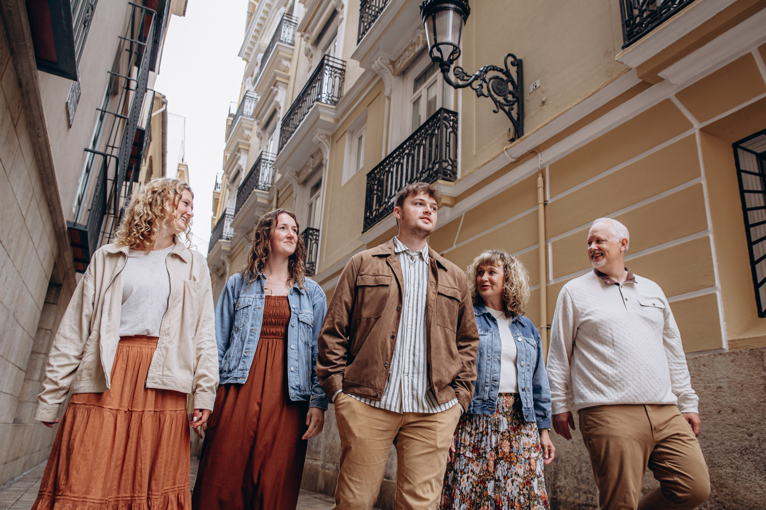 Familia multigeneracional caminando de la mano por una calle antigua de Valencia, España, durante una sesión familiar espontánea. Captura de momentos auténticos, arquitectura histórica y conexión alegre — inspiración perfecta para quienes buscan sesiones familiares en Valencia y en toda España.