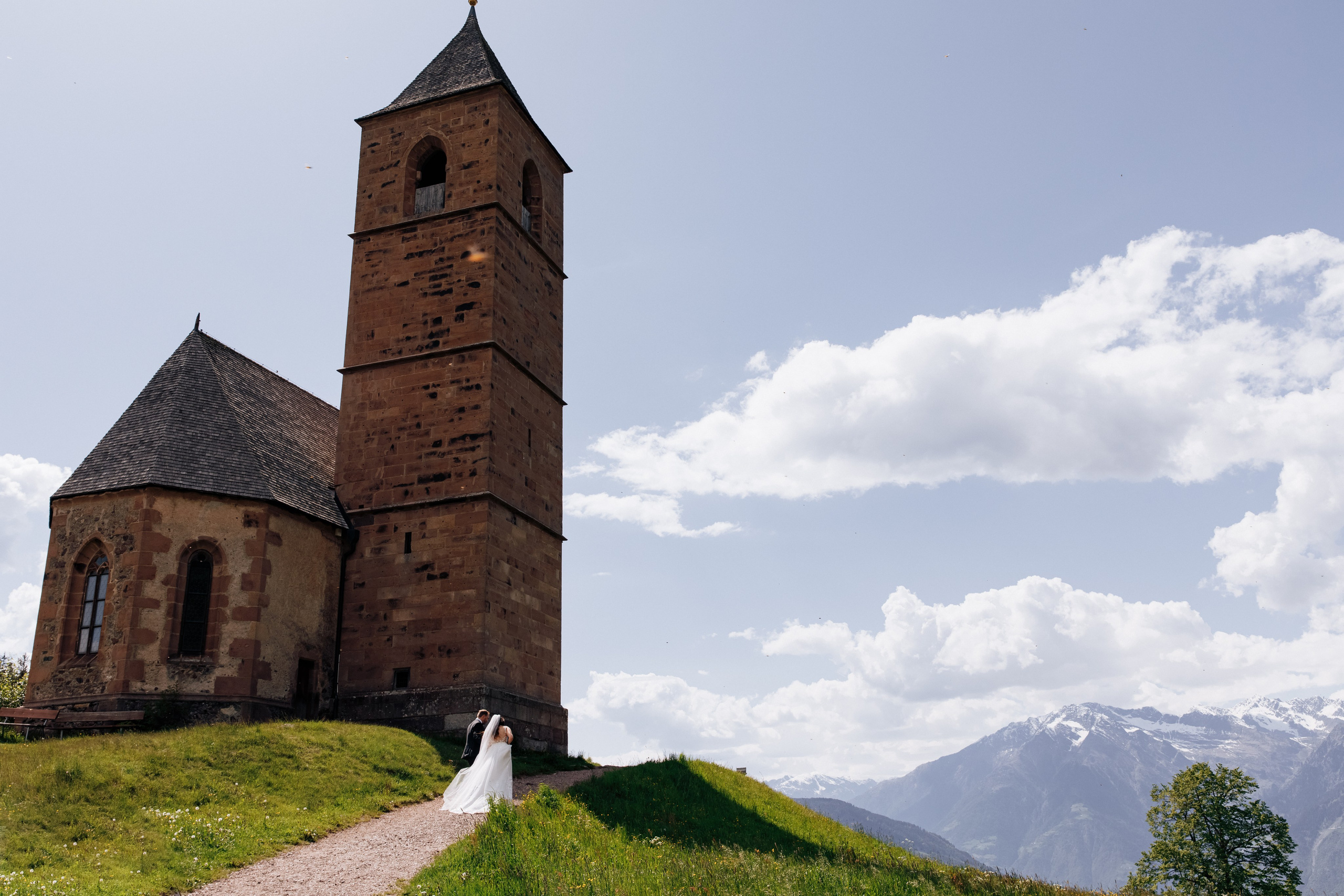 Der Bräutigam führt die Braut an der Hand zur St. Kathrein-Kirche in Hafling, ein romantischer Moment auf dem Weg zur Zeremonie.