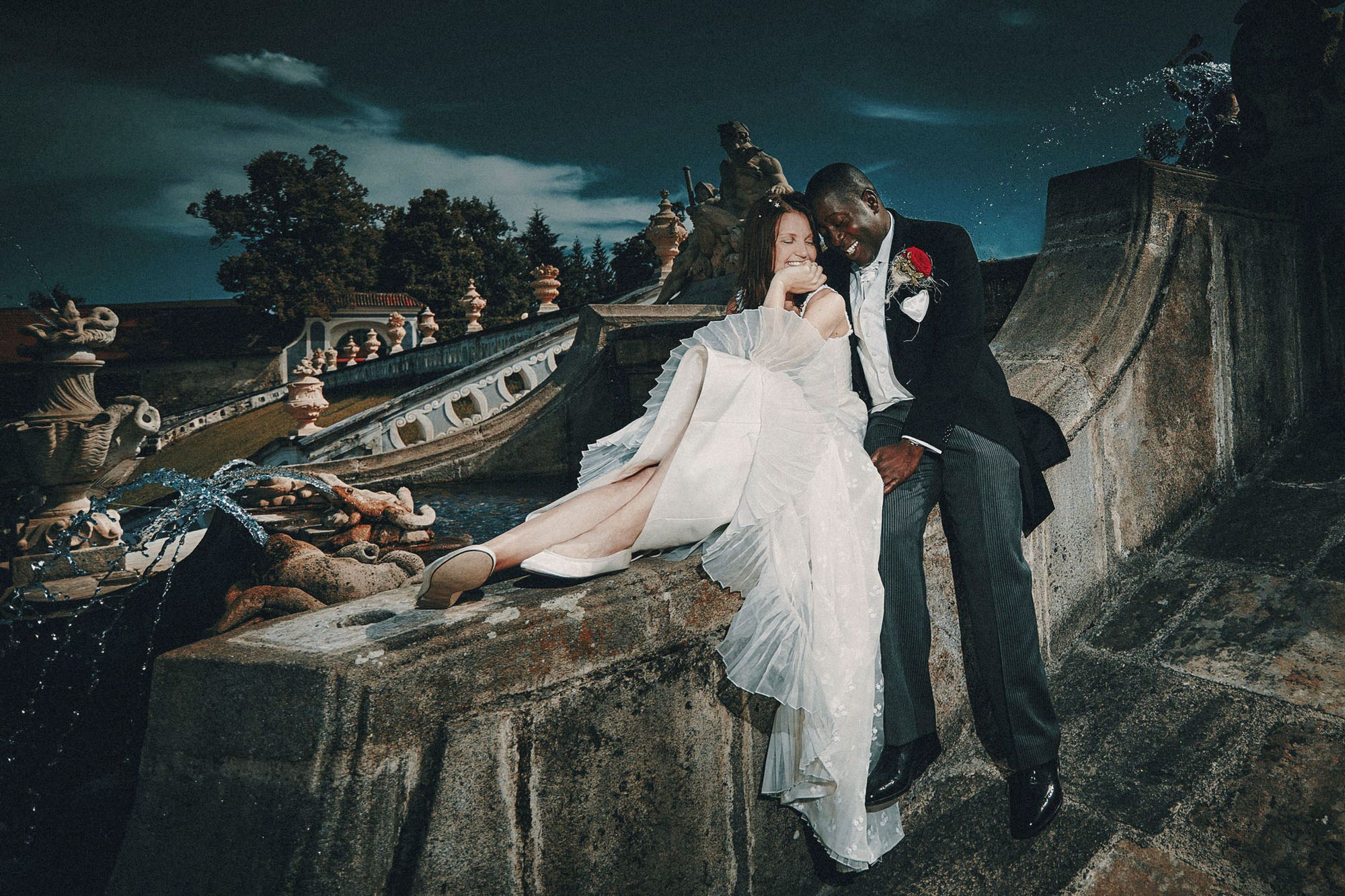 Smiling bride with flowing dress next to delighted English groom in Cesky Krumlov Castle garden