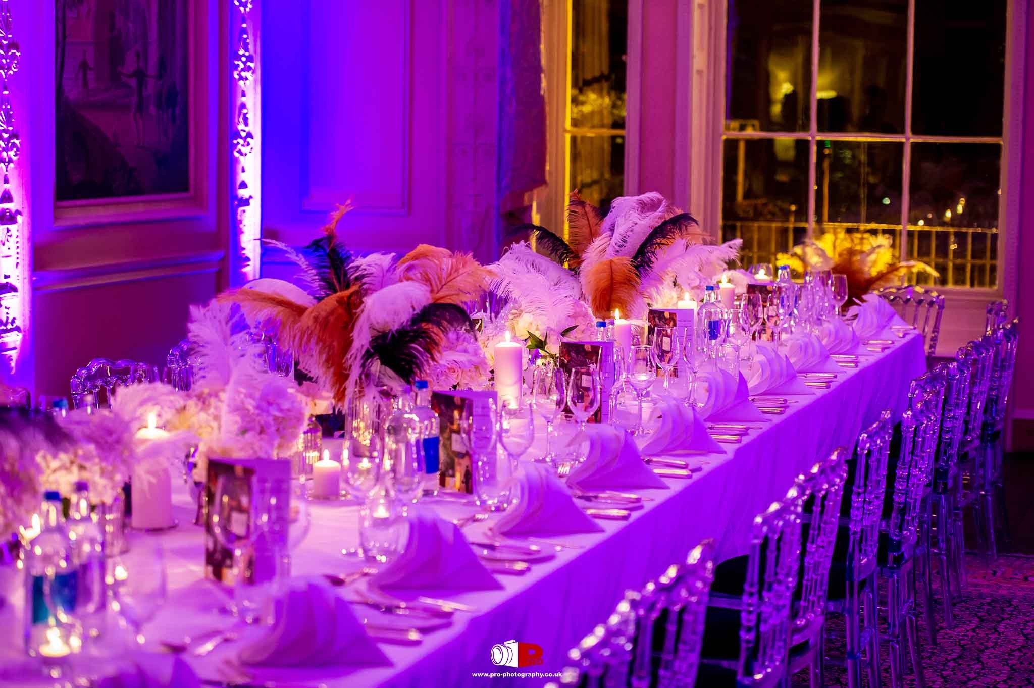 An elegant dining setup with candles, feathers, and purple lighting at a high-end event.