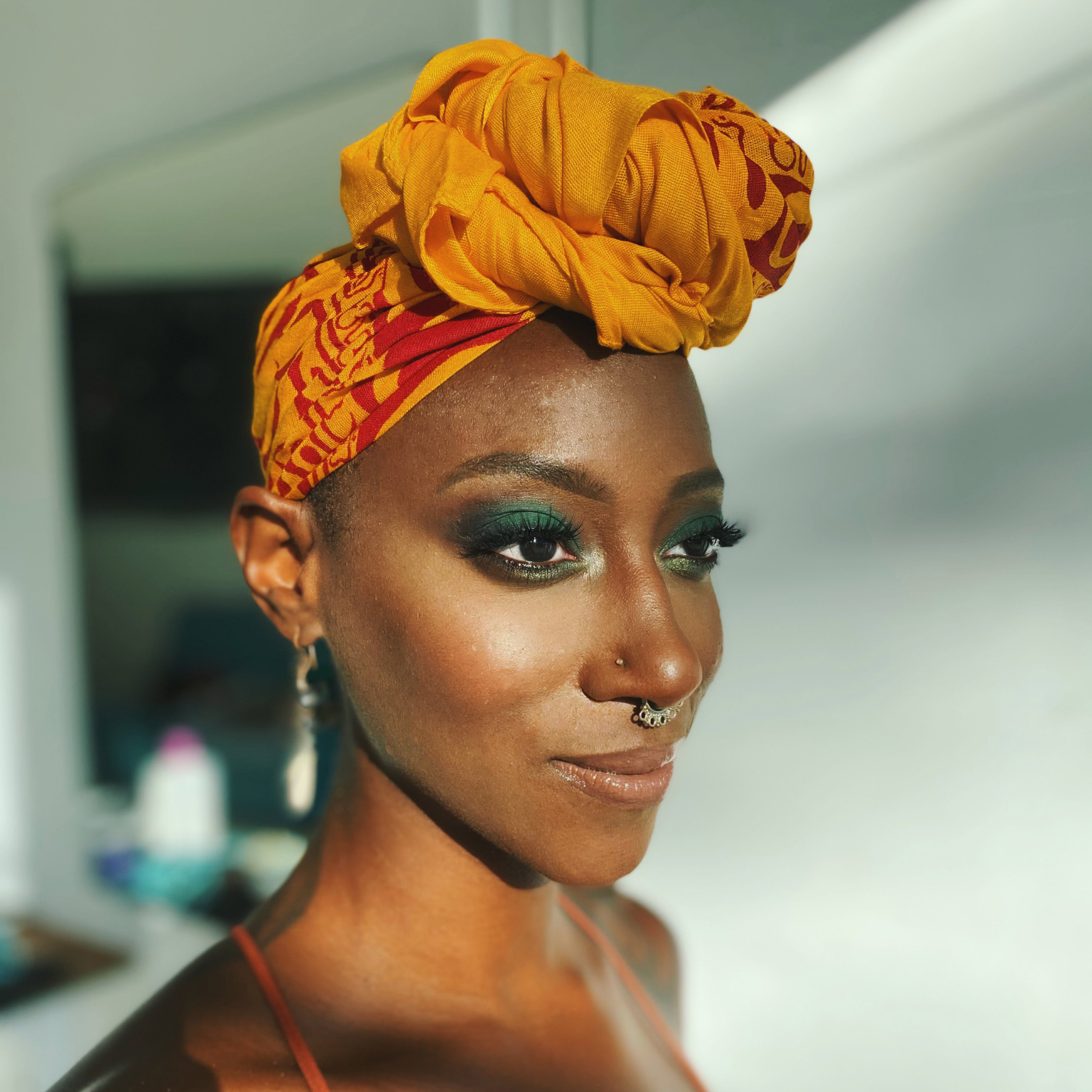 black woman with bright green smoky eyes makeup and orange turban 