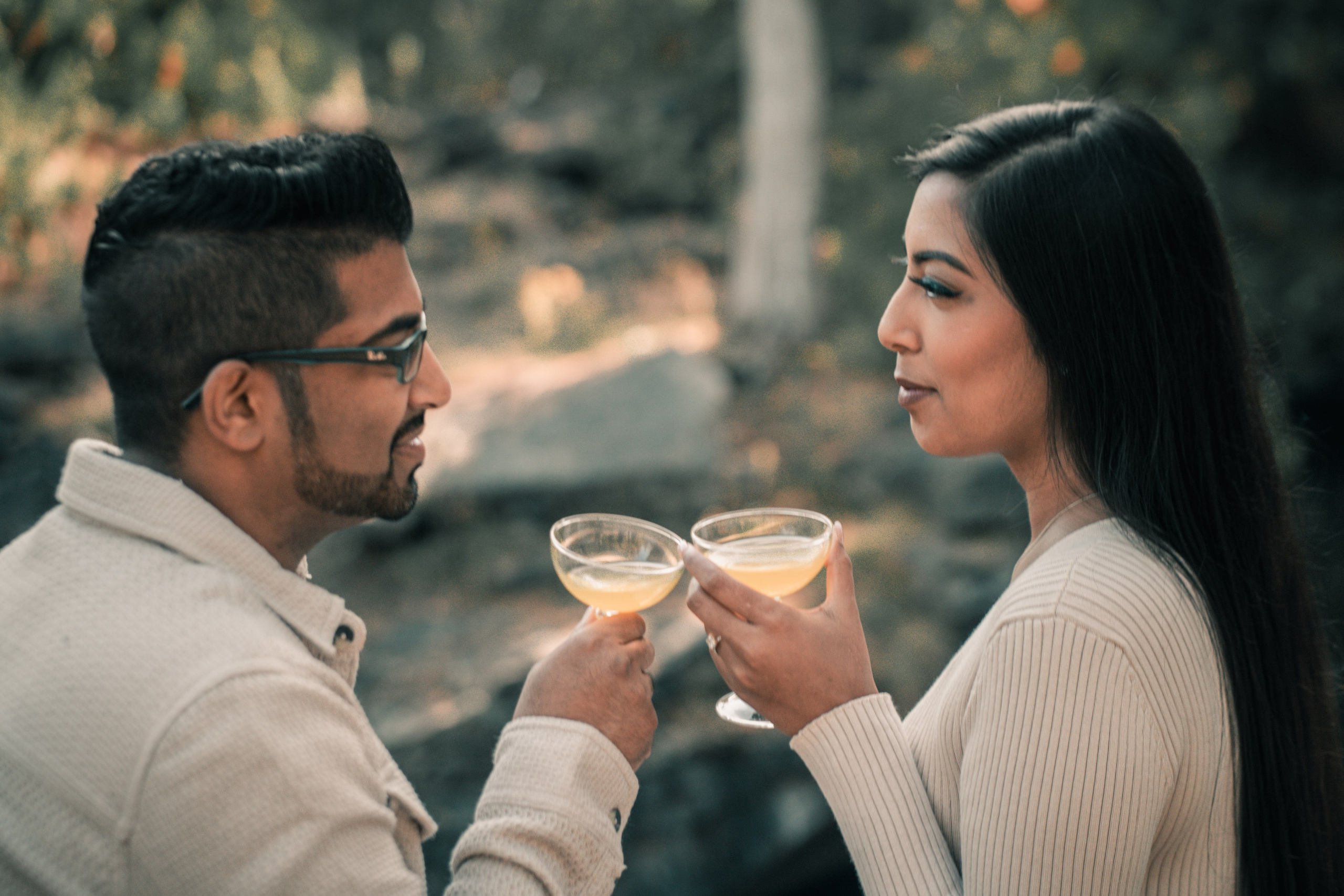 Engaged couple standing together in a sunlit garden, holding hands and smiling during a romantic engagement photoshoot.