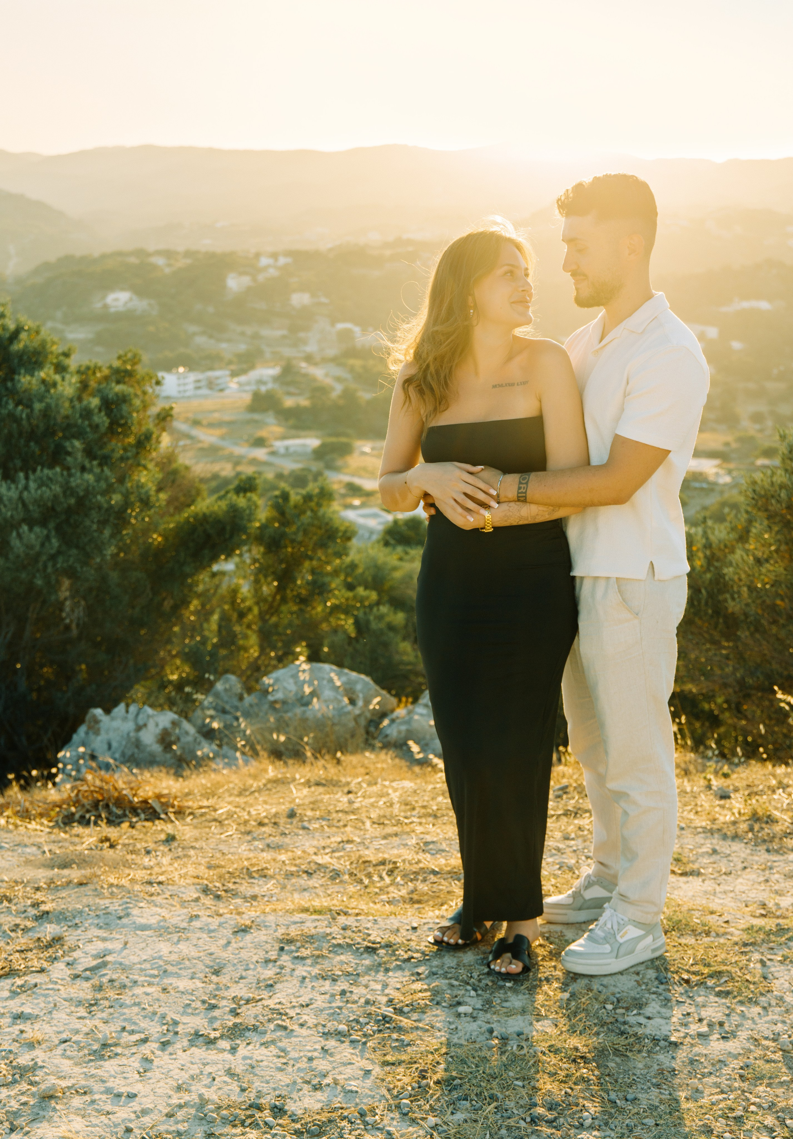 "Liebevoller Blickkontakt: Ein Paar auf dem Felsplateau des Profitis Ilias vor der Kulisse von Faliraki und dem Mittelmeer."