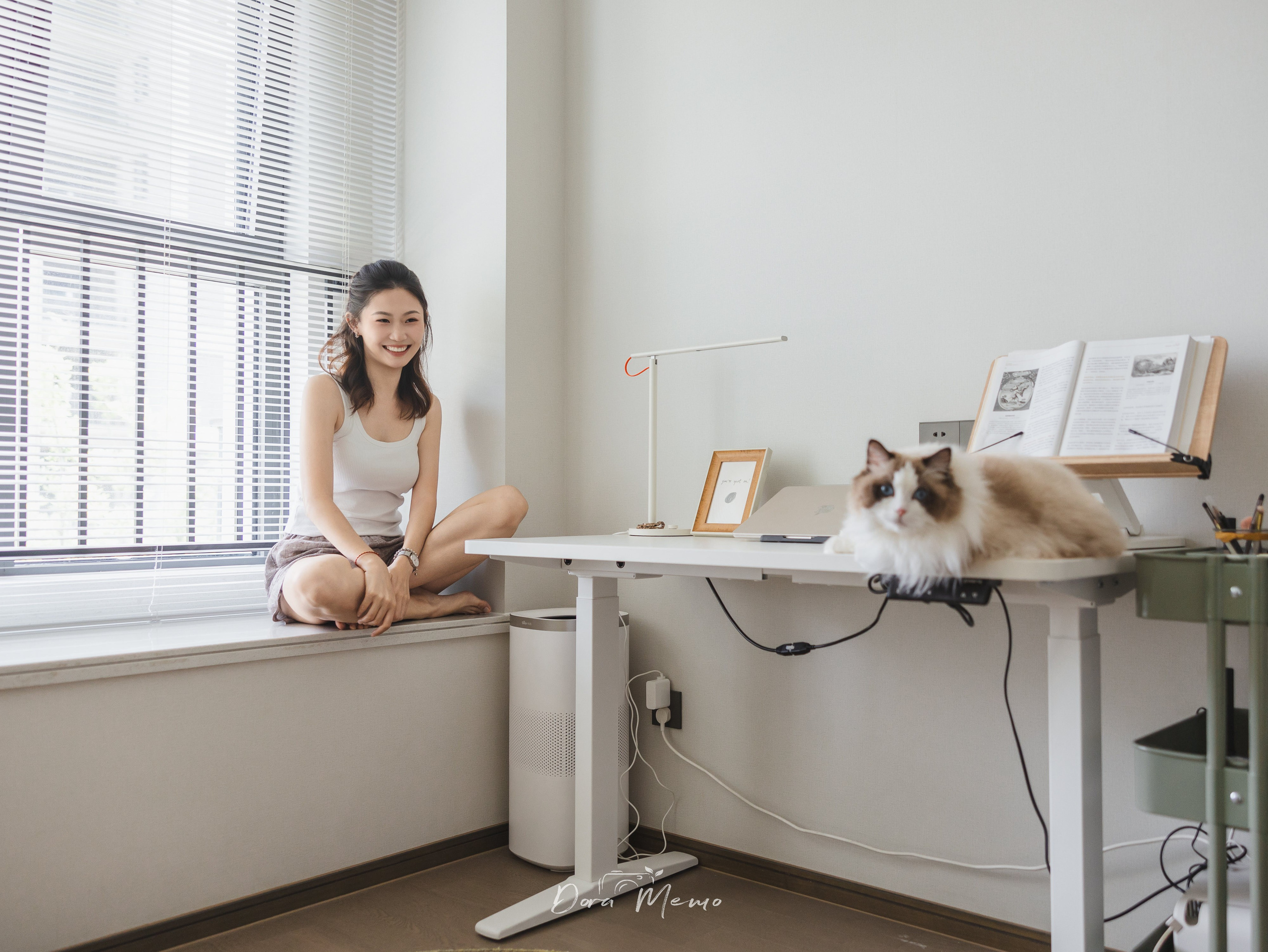 A woman sits by the window while her cat lounges on a nearby desk — a calm, minimalistic in-home pet lifestyle session in Shanghai.