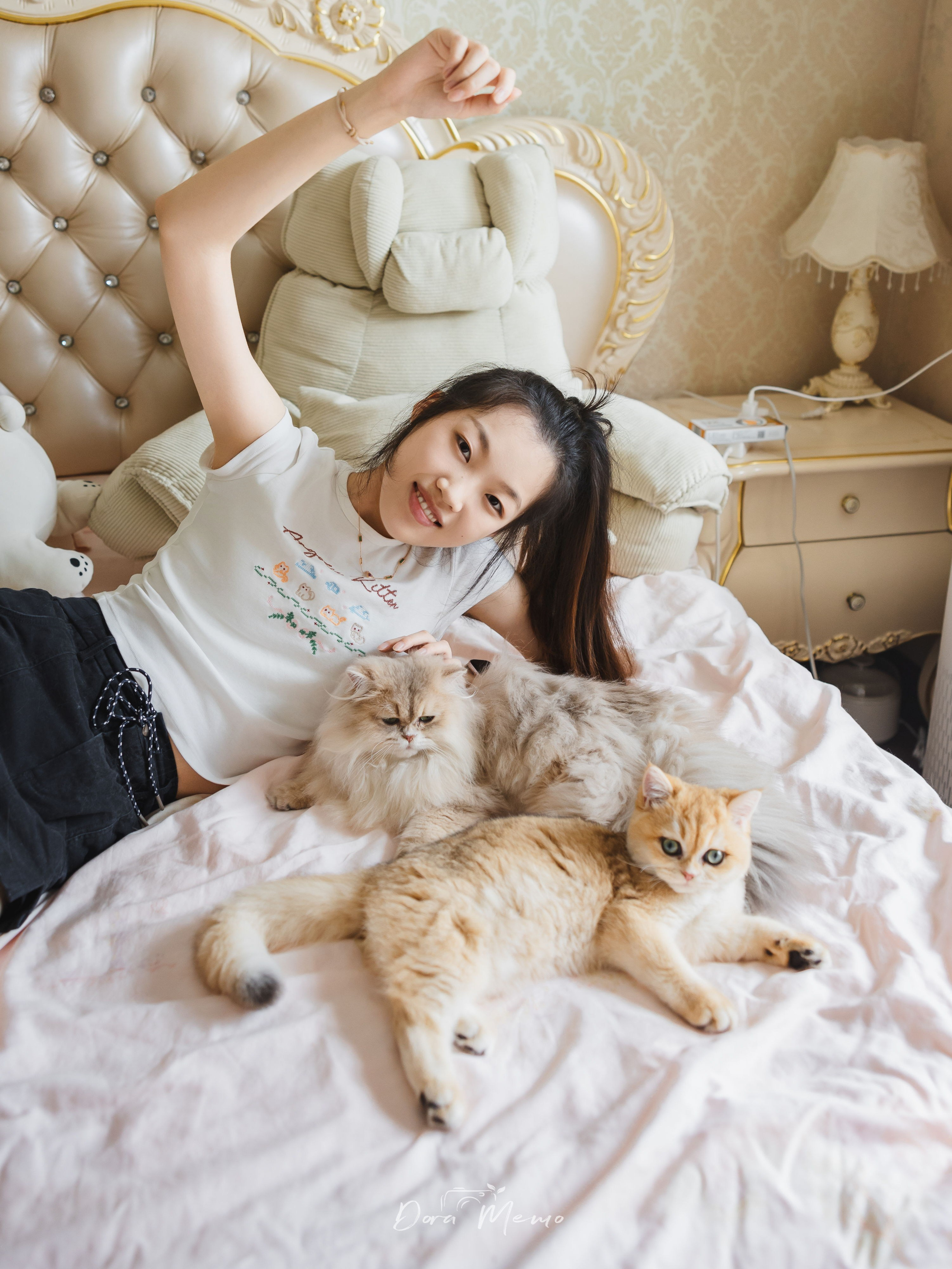 A woman lies on the bed with her two cats during a relaxed pet family session.