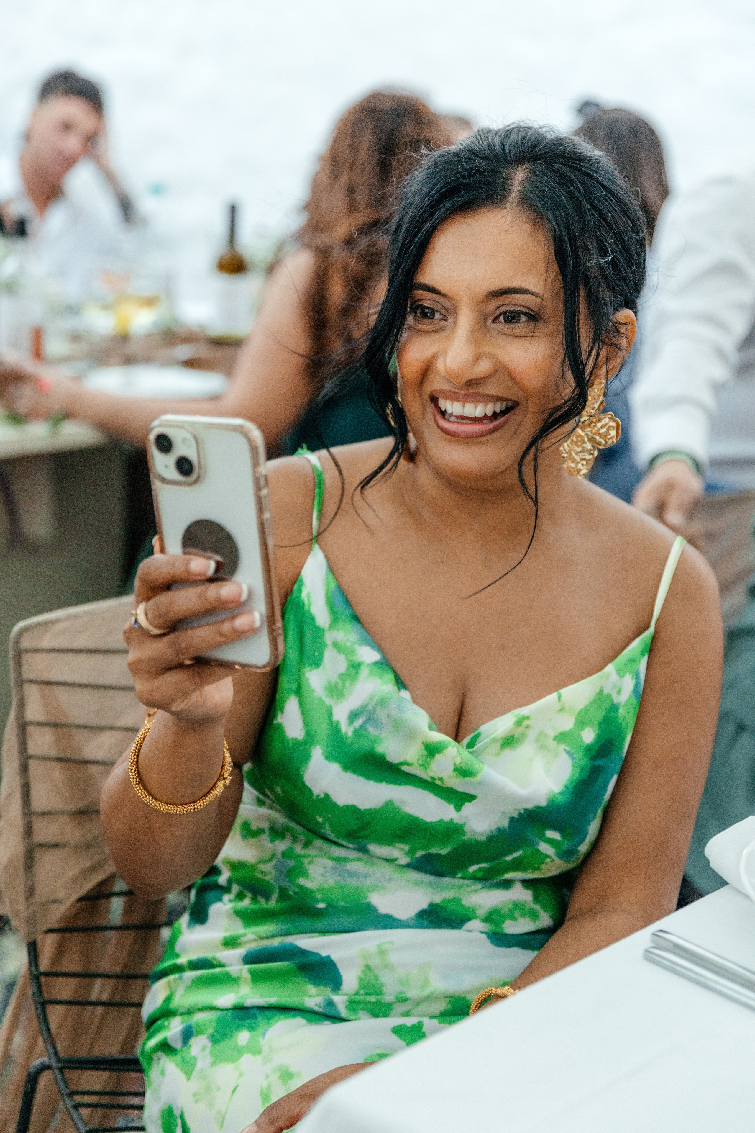 The guest  is laughing and recording a video during a humorous wedding speech by her brother at a charming restaurant in Lindos, Greece.