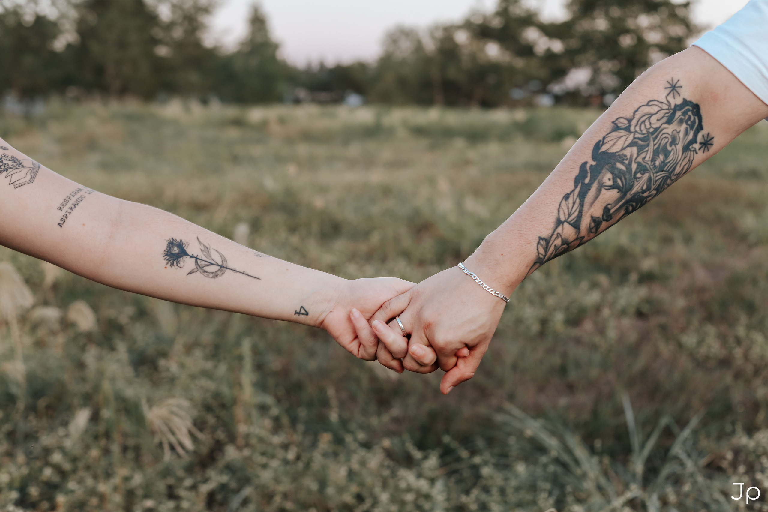 Detalhe das mãos dadas com tatuagens visíveis.