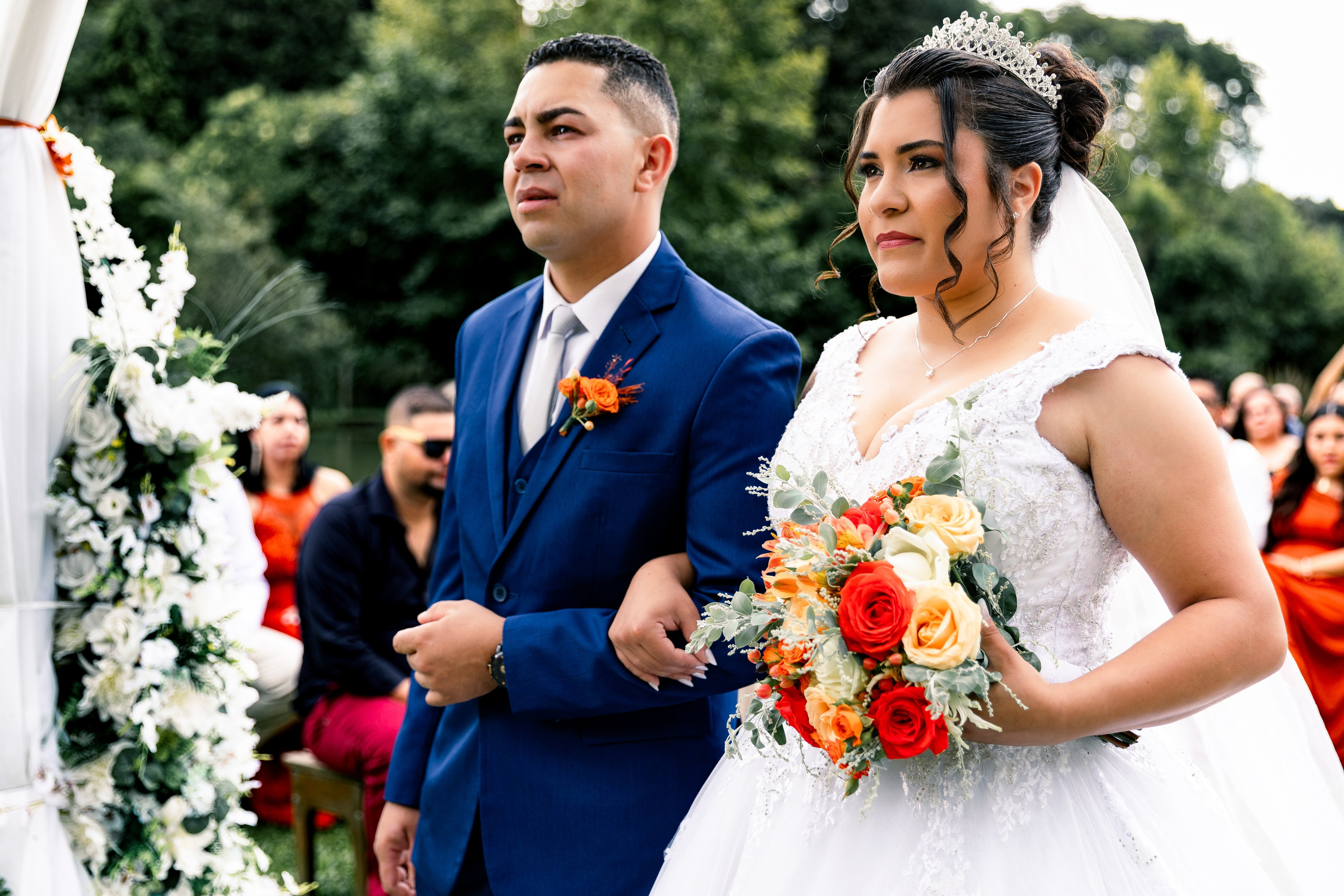Casal posicionado no altar decorado com flores, prestes a trocar os votos matrimoniais.