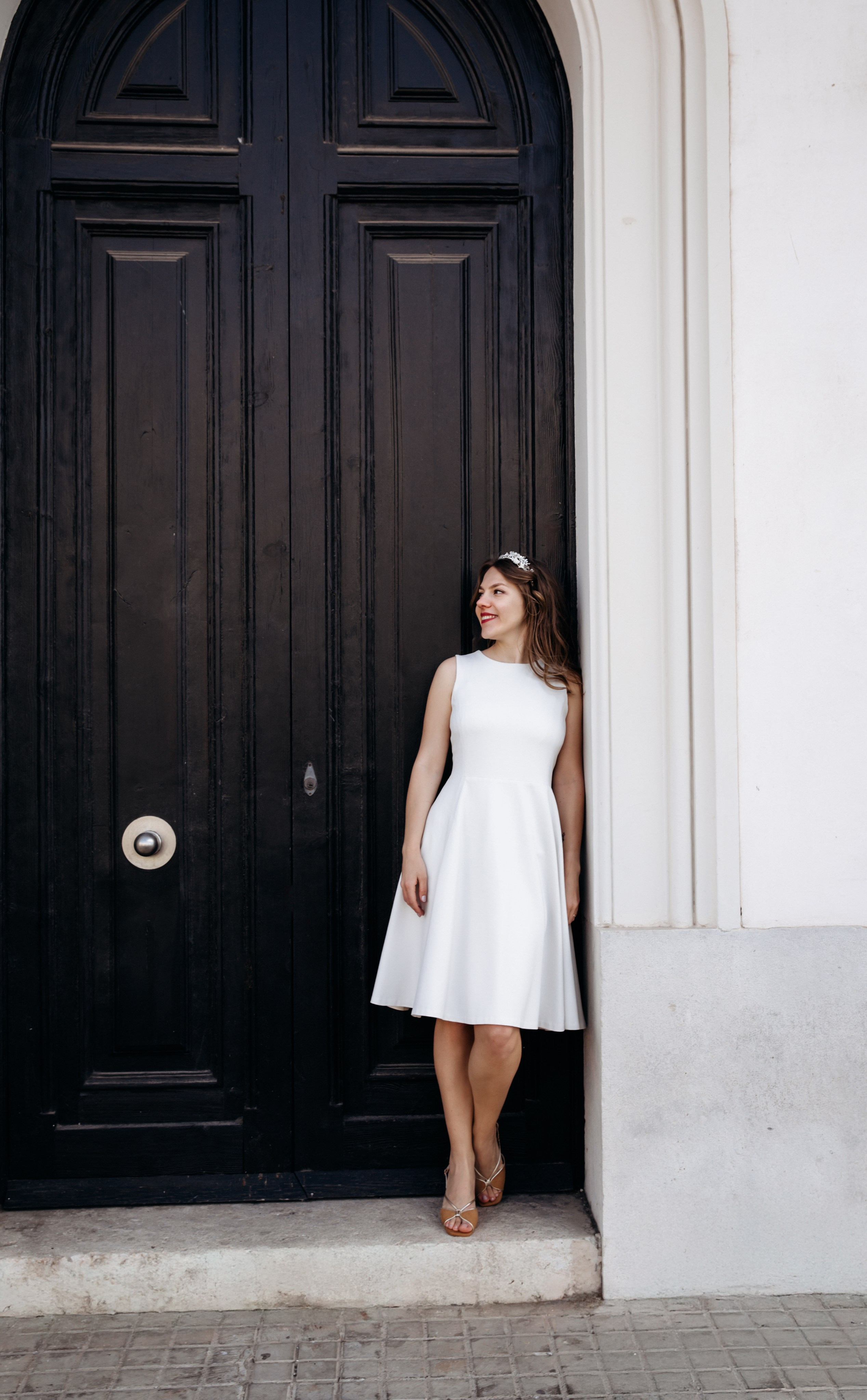 Stylish bride in a white dress poses against an elegant black door in Madrid, Spain — a modern and artistic bridal portrait capturing timeless beauty and architectural charm. Perfect for those seeking chic and creative wedding photoshoots in Madrid and across Spain.