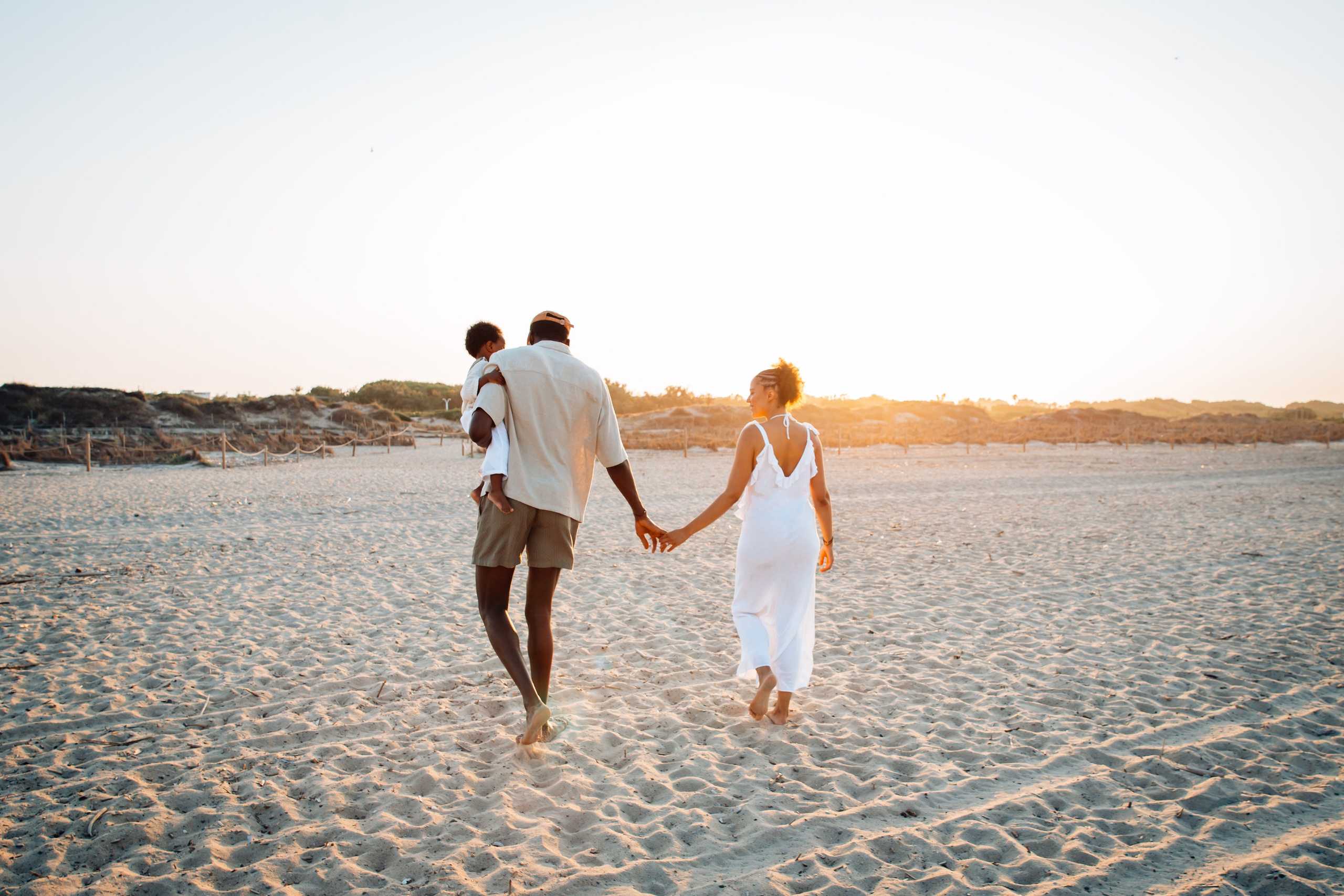 Sesión fotográfica familiar al atardecer en la playa de Calpe, España — padres descalzos caminando de la mano con su hijo junto a la orilla, capturando momentos relajados y naturales.