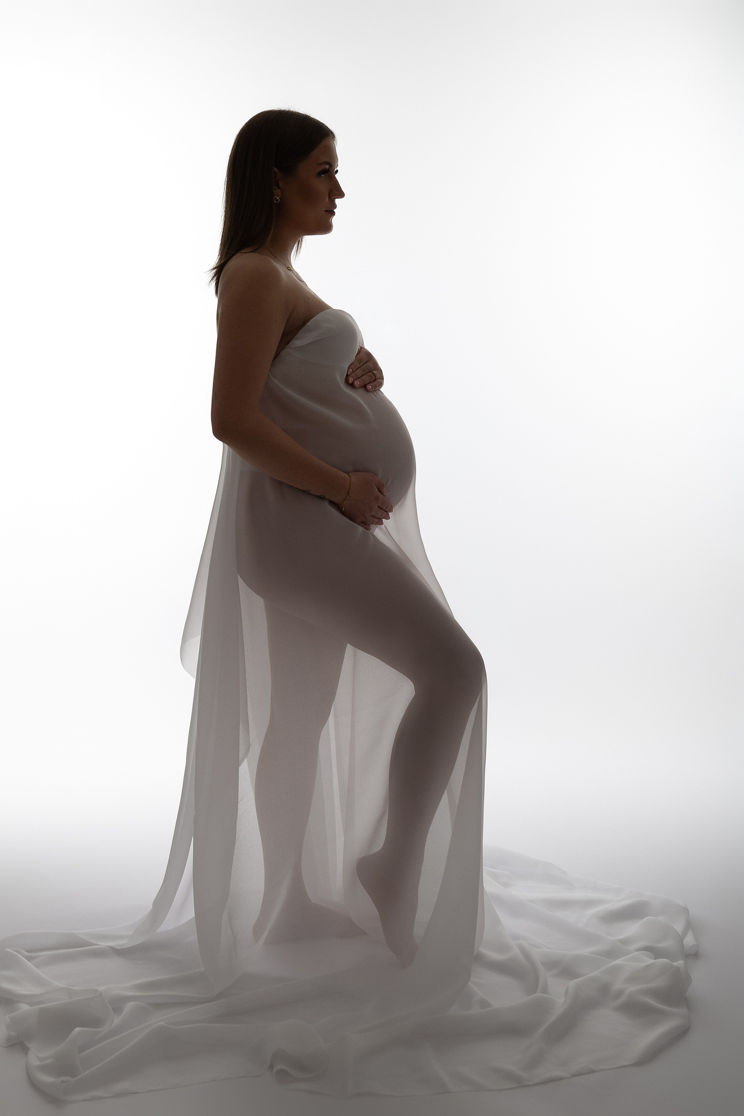 Künstlerisches Schwangerschaftsfoto mit fließendem Stoff in sanftem Licht