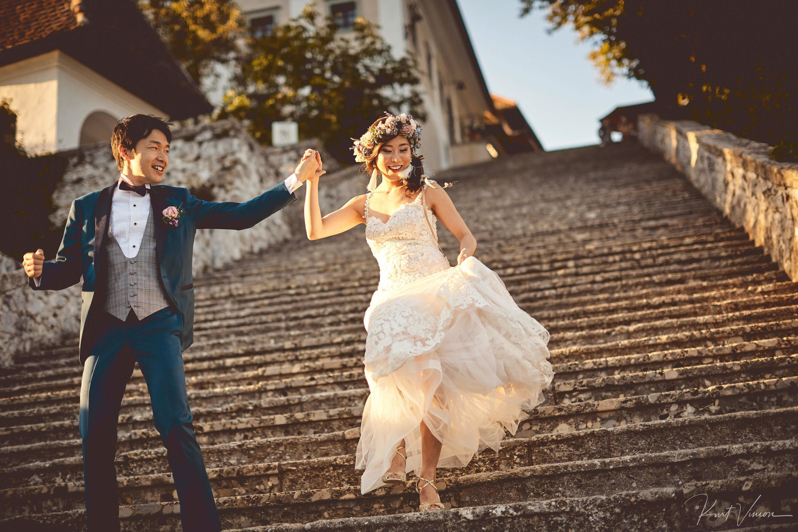 Newlyweds celebrating arms high descending Bled Island 99 steps.