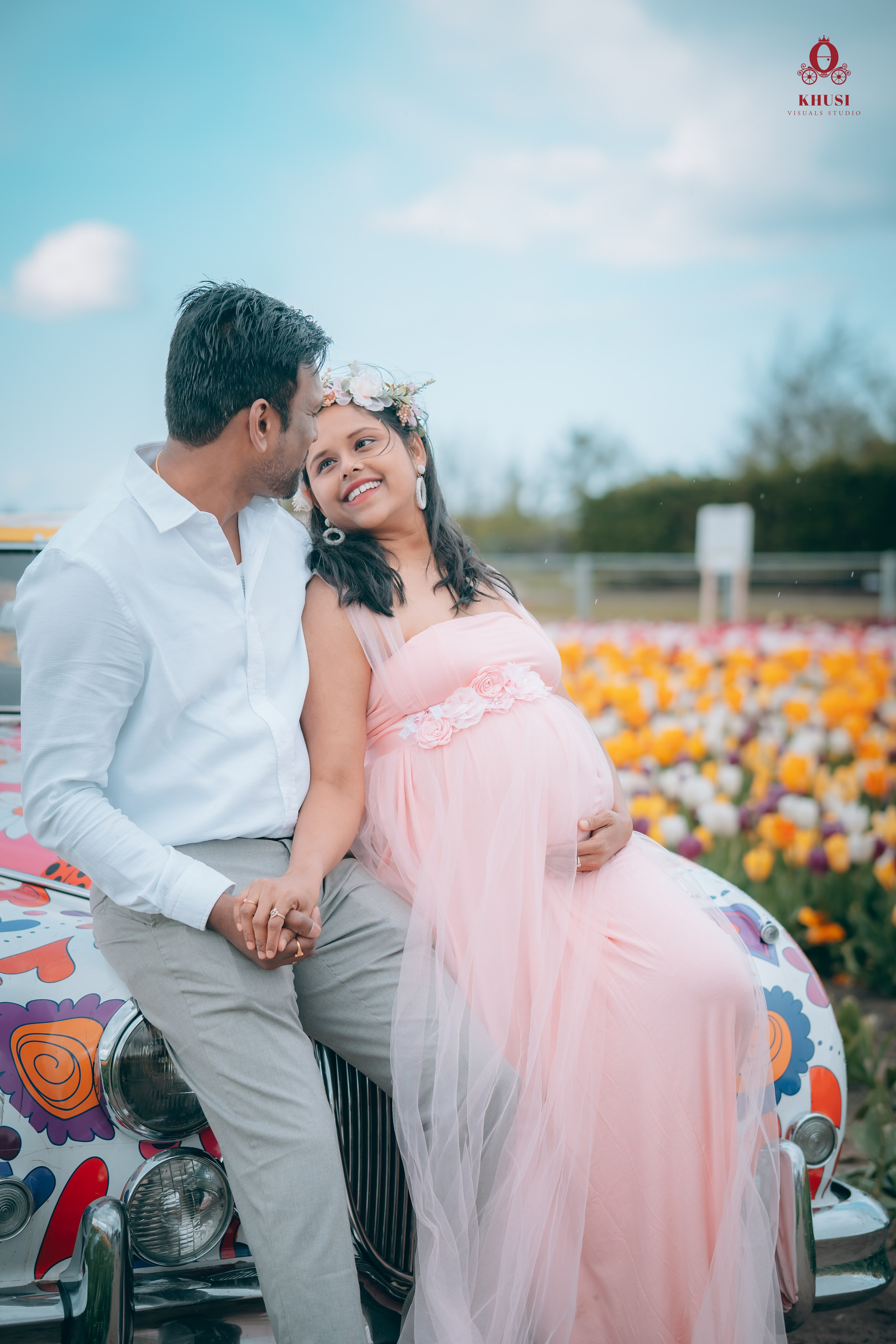 A pregnant woman leaning on her husband and sitting infront of a car in tulip flower field in Netherlands