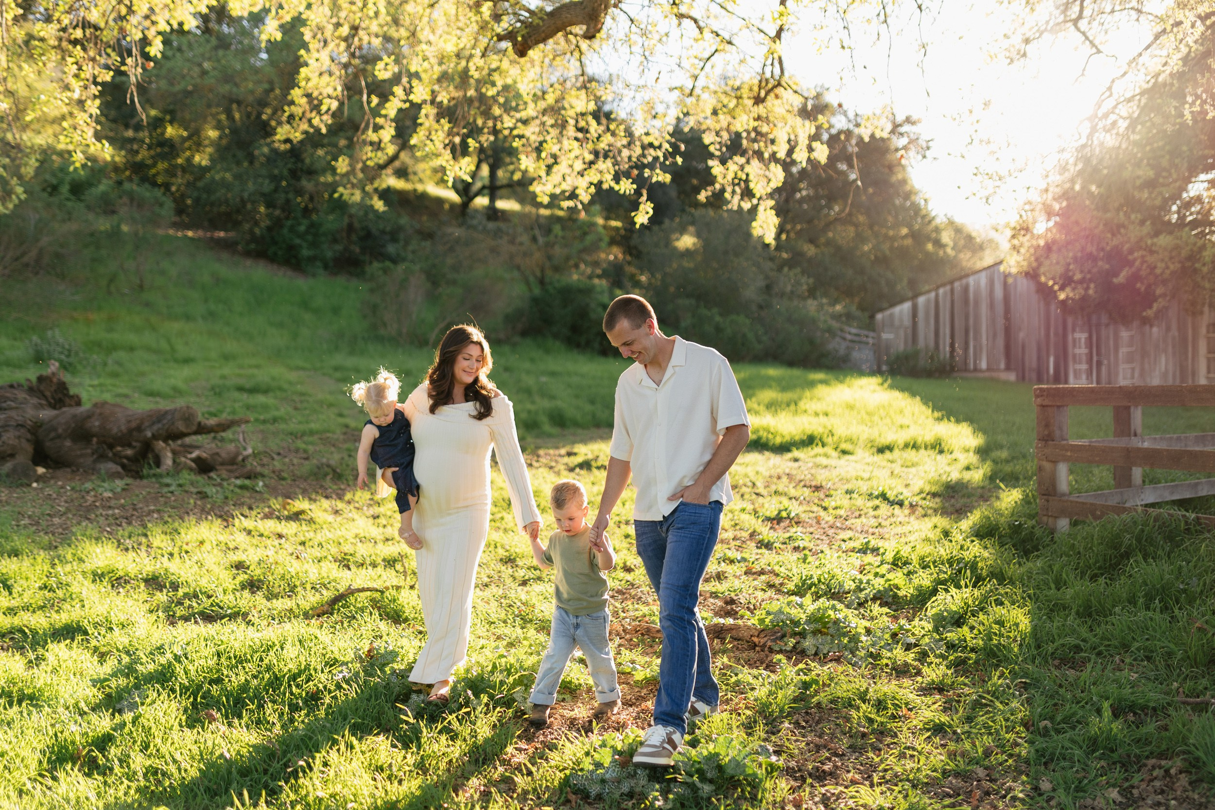 Family of four expecting third baby walking together in a green park in San Jose California during a lifestyle maternity photoshoot