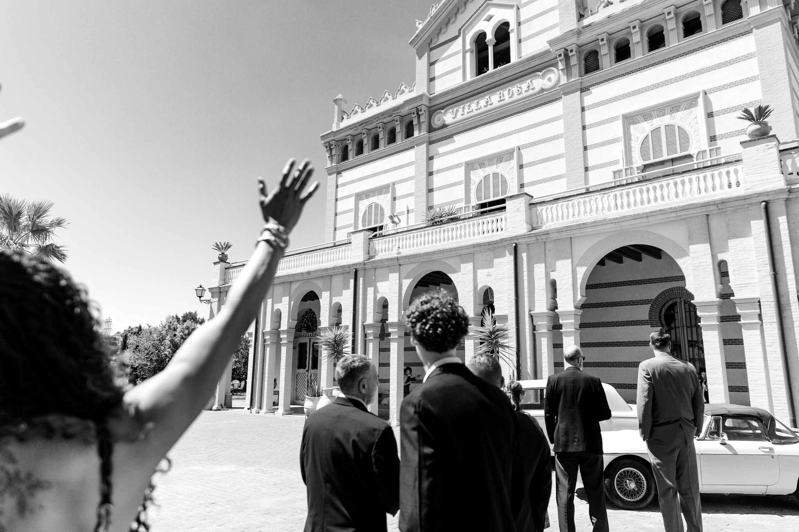 The bride waves to guests from a balcony before the wedding ceremony in a beautiful destination venue in Spain. 
