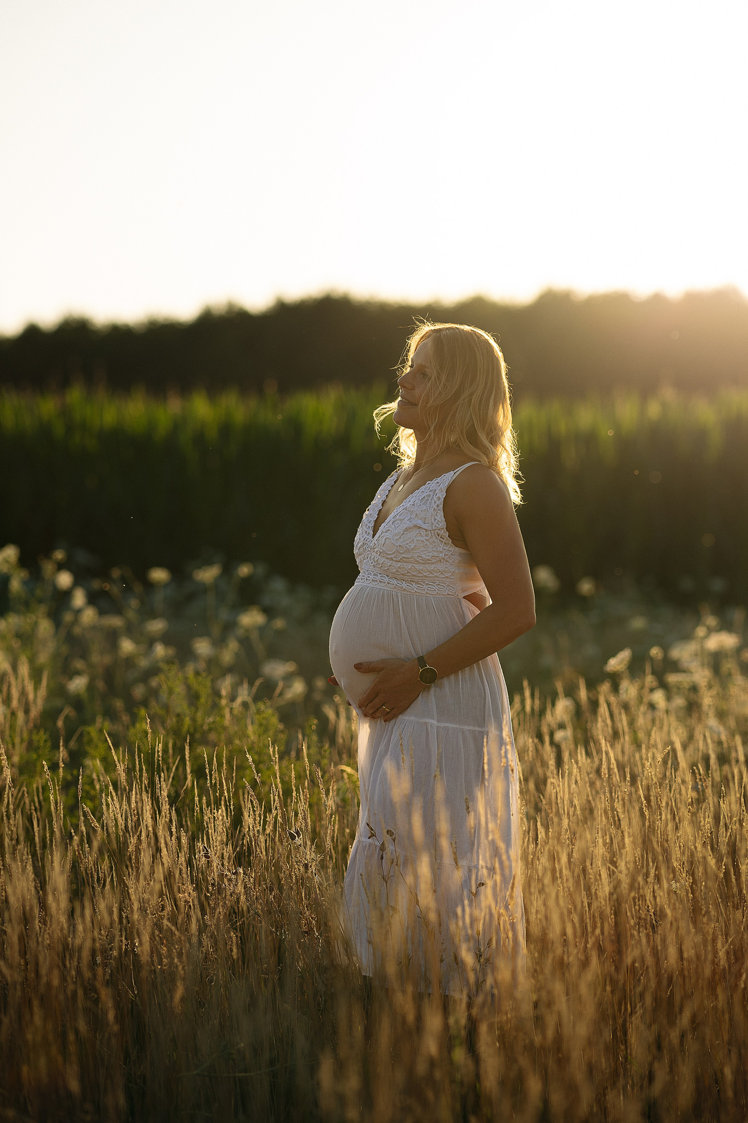 Schwangere Frau im goldenen Abendlicht bei einem emotionalen Babybauch Fotoshooting in der Natur.