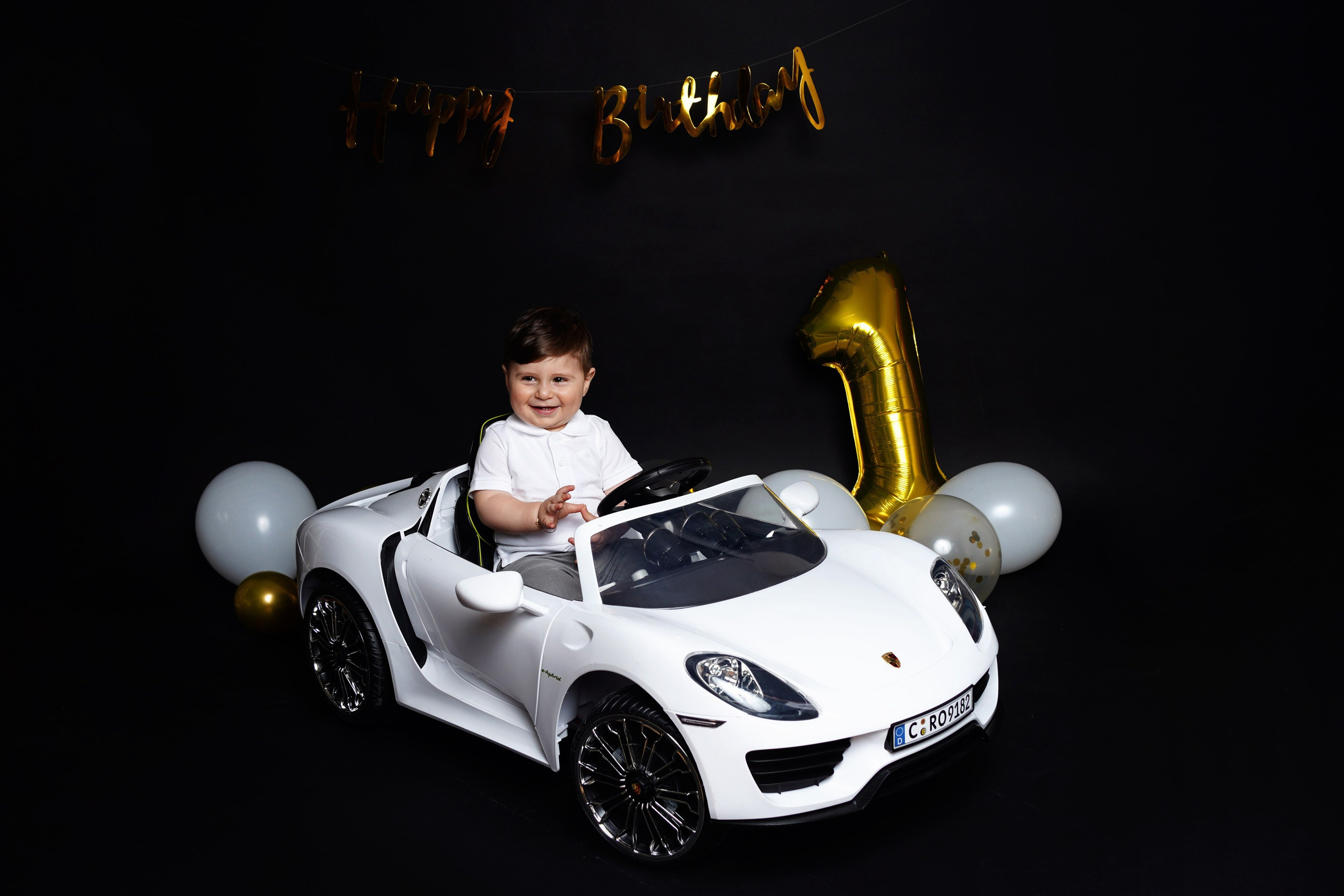Junge im weißen Spielzeugauto vor schwarzem Hintergrund mit goldener Zahl 1 – Gersthofen