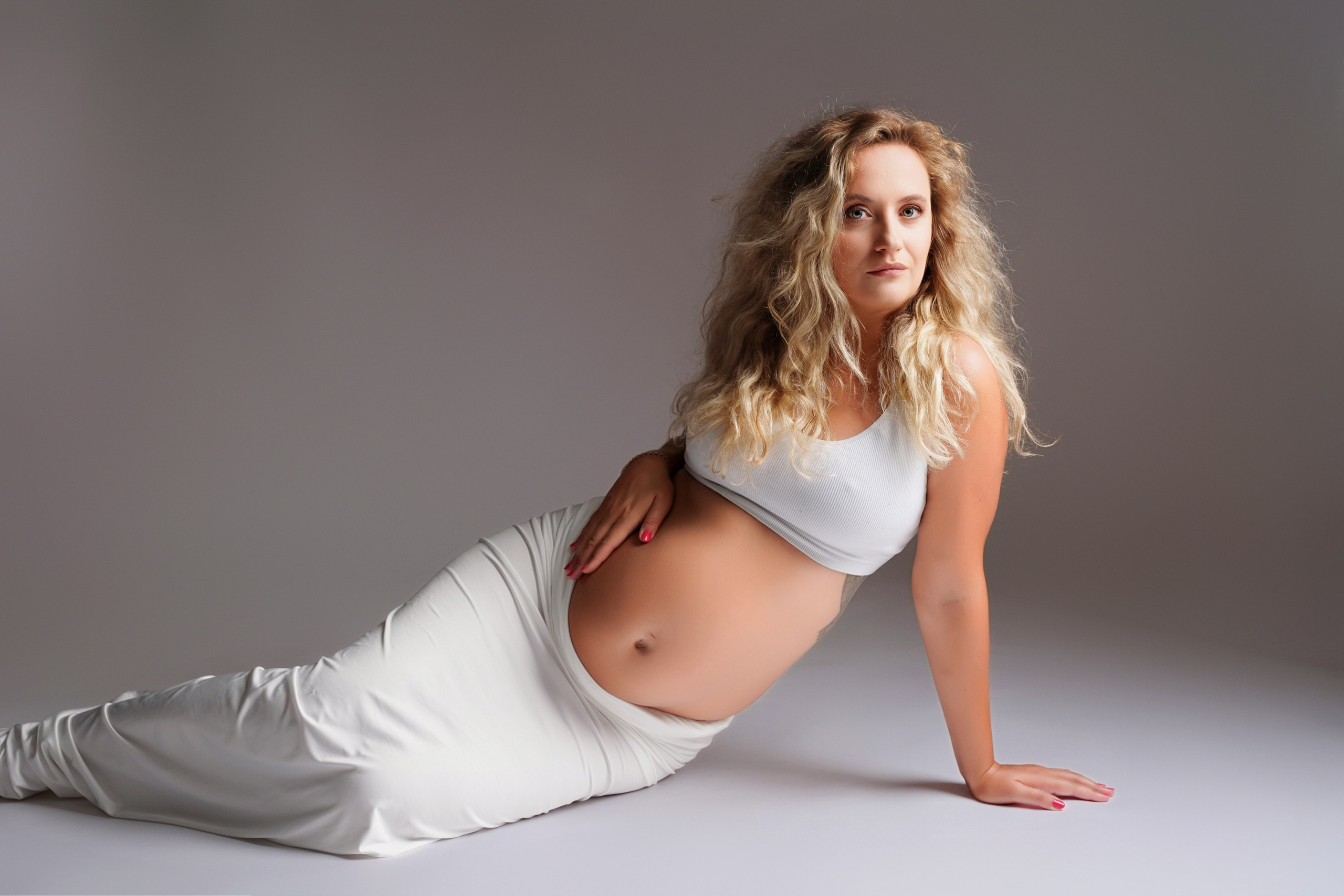 Fröhliche schwangere Frau im weißen Outfit im hellen Fotostudio – Gersthofen