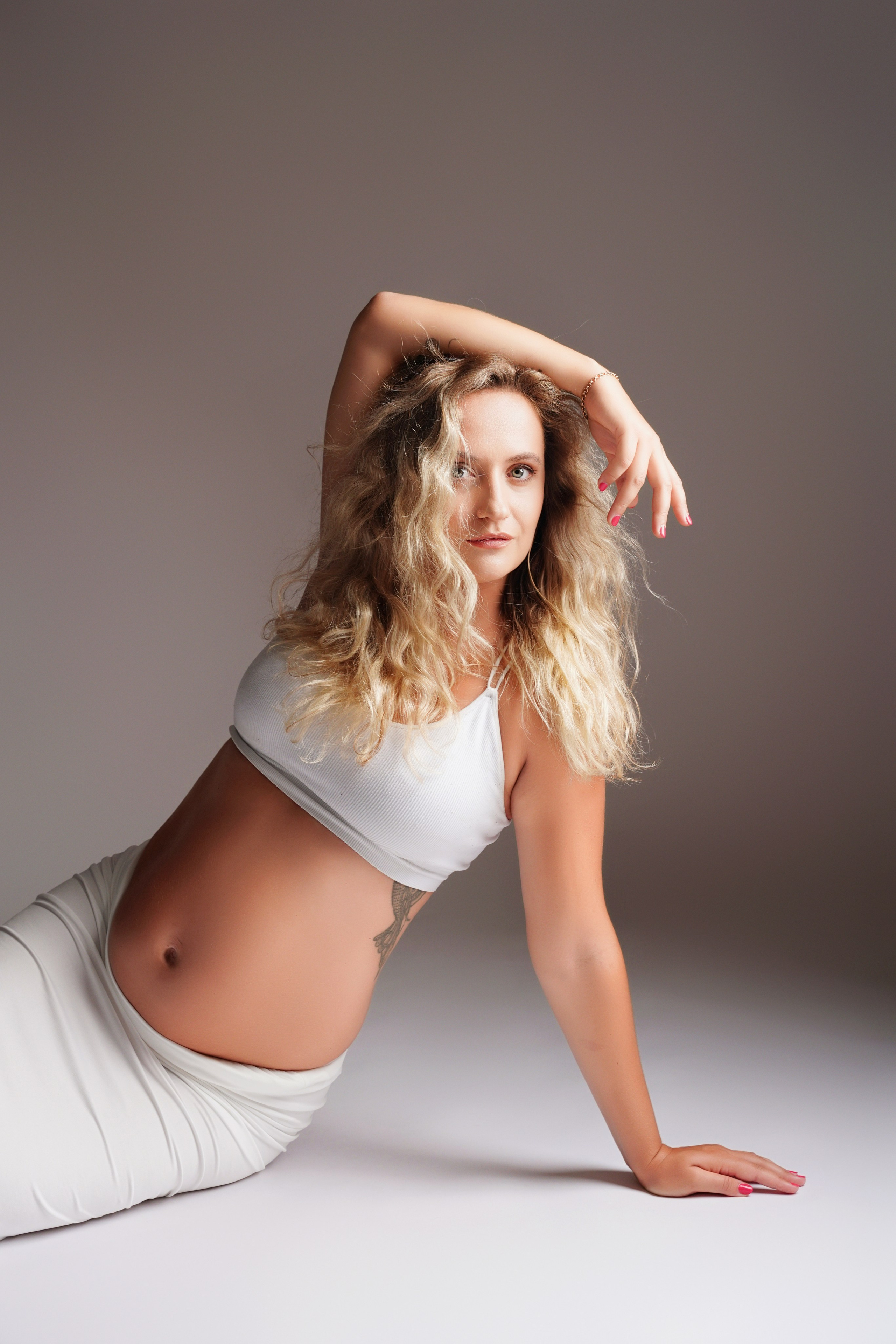Schwangere Frau posiert liegend im weißen Zweiteiler – Babybauch Fotostudio Augsburg
