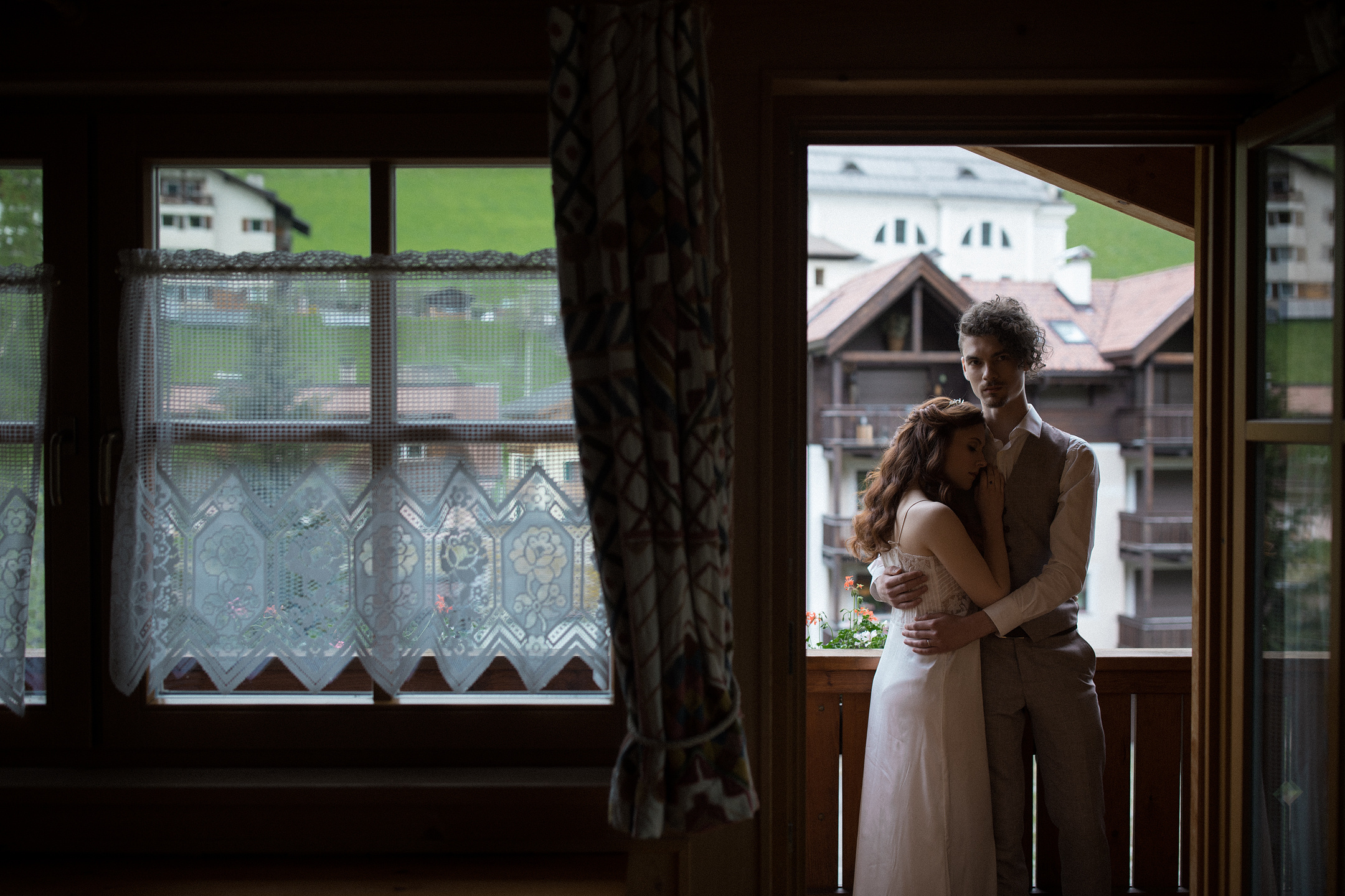 Paar umarmt sich drinnen mit Dolomiten-Bergdorfblick