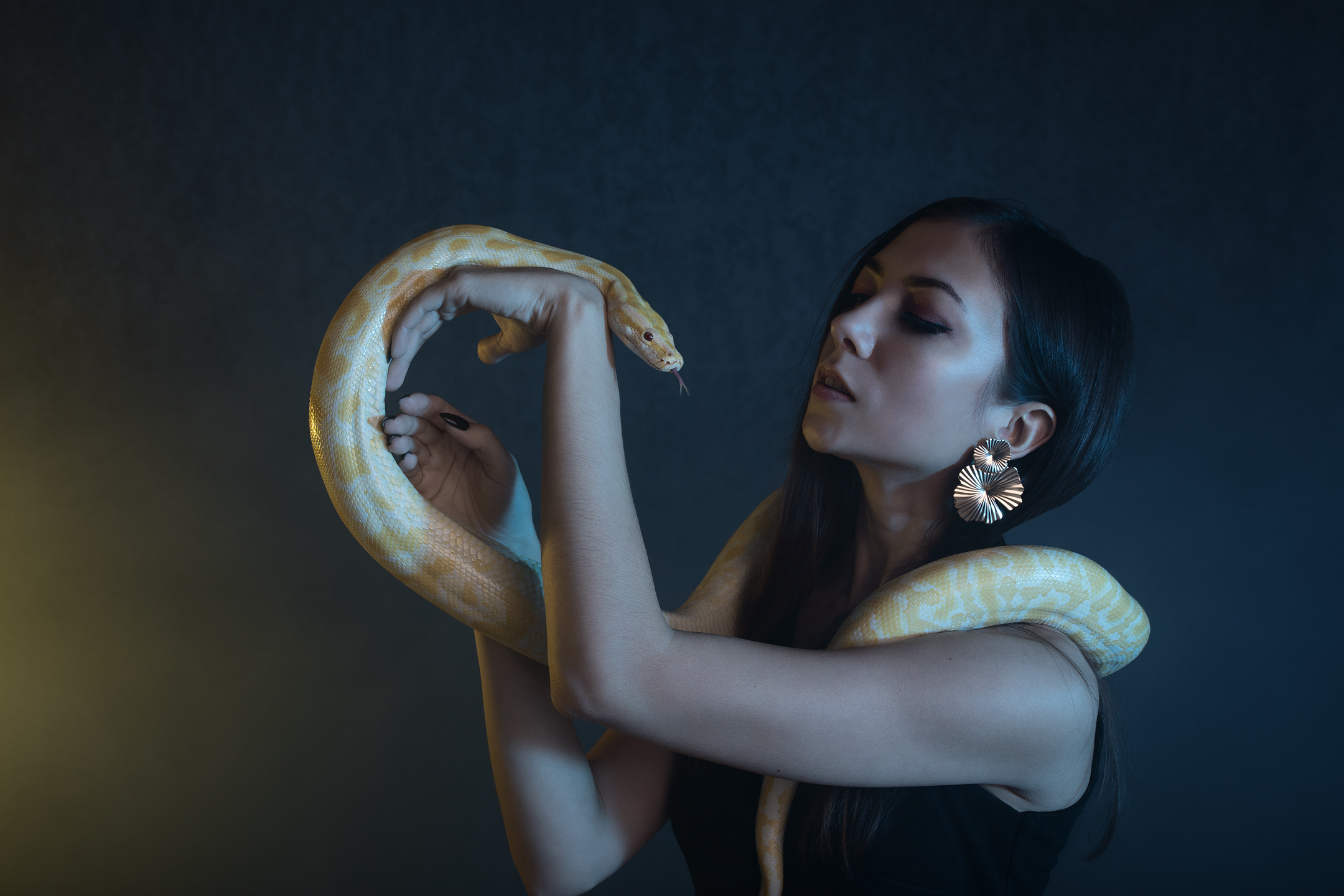Profile view of woman with python around her arms — dramatic lighting