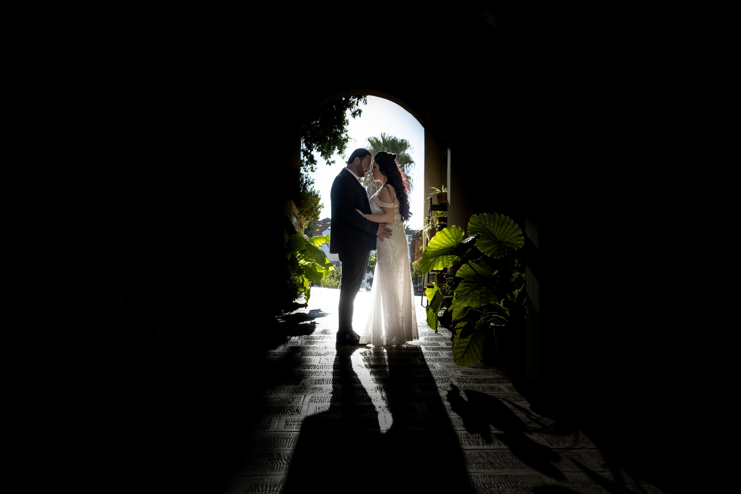 Bride and groom in silhouette, standing in a doorway surrounded by lush greenery.