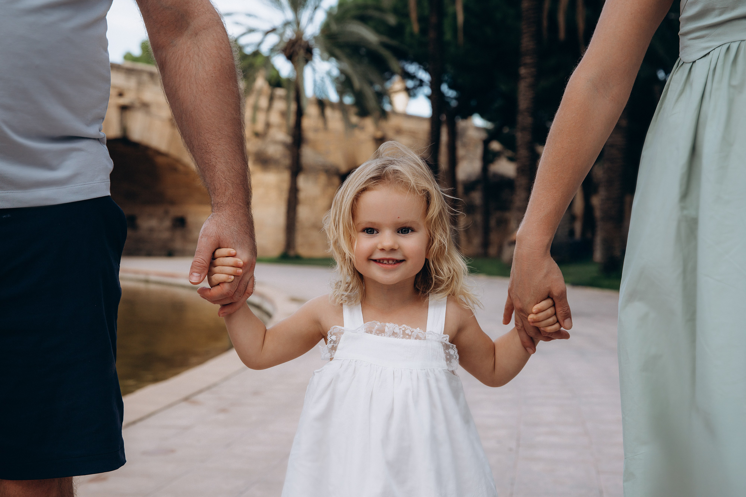 Niña sonriente tomada de la mano de sus padres durante una alegre sesión de fotos familiar en Valencia, España — una escena ideal para quienes buscan sesiones fotográficas familiares cálidas y llenas de amor en Valencia y en toda España.