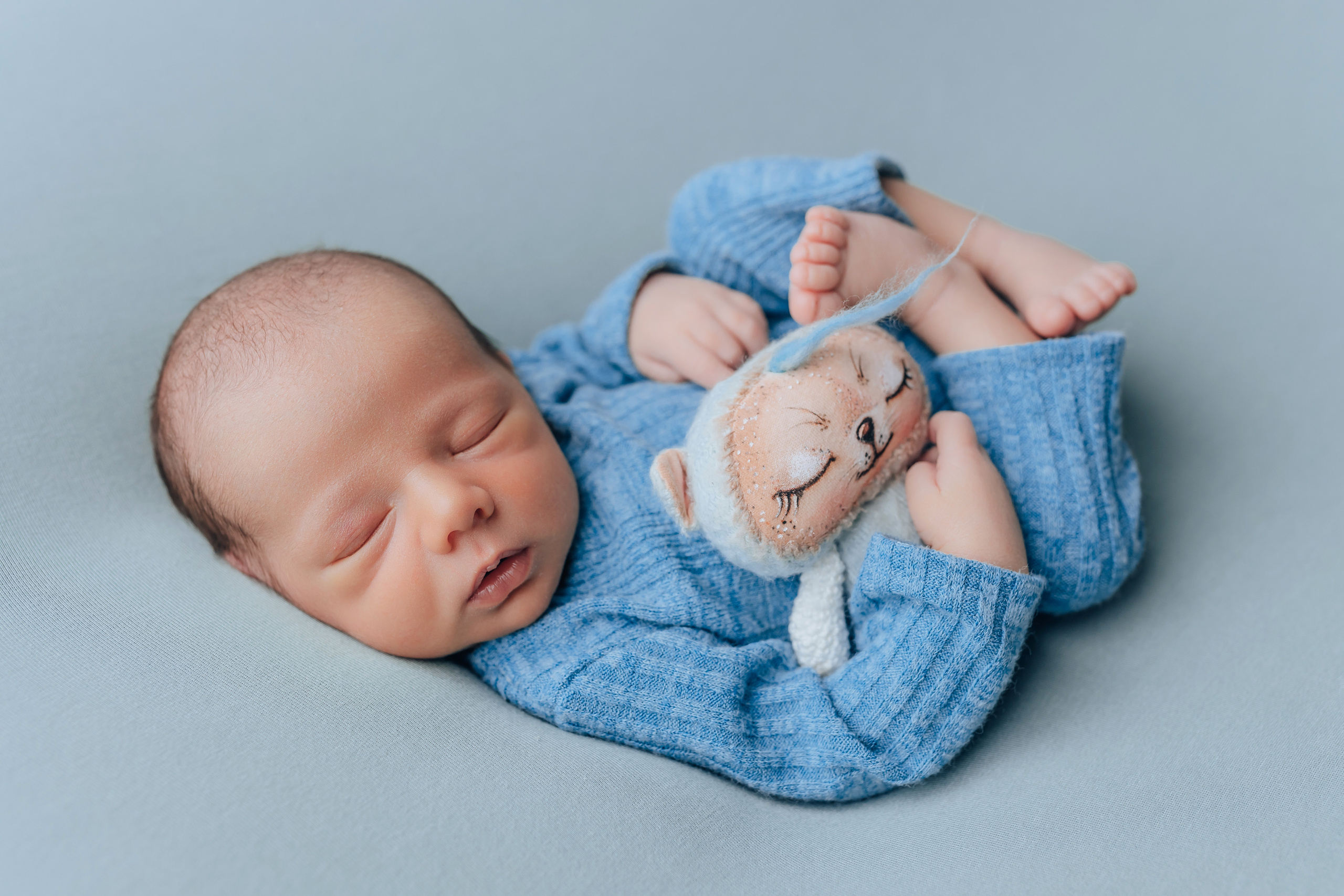 Neugeborenenfotografie in München – Babyjunge mit Stofftier auf blauem Hintergrund