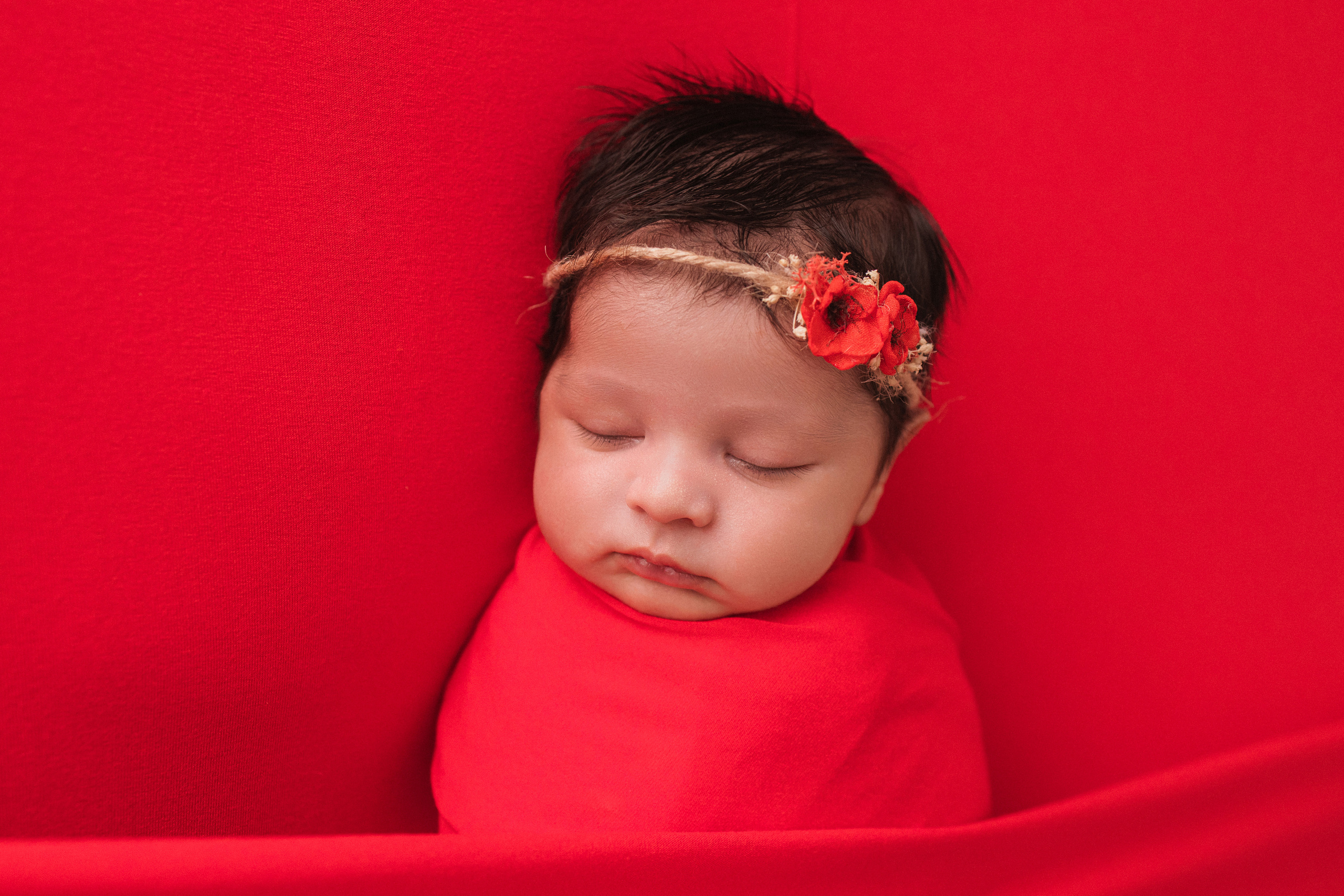 Neugeborenenfotoshooting auf rotem Hintergrund – Baby mit Blumenstirnband