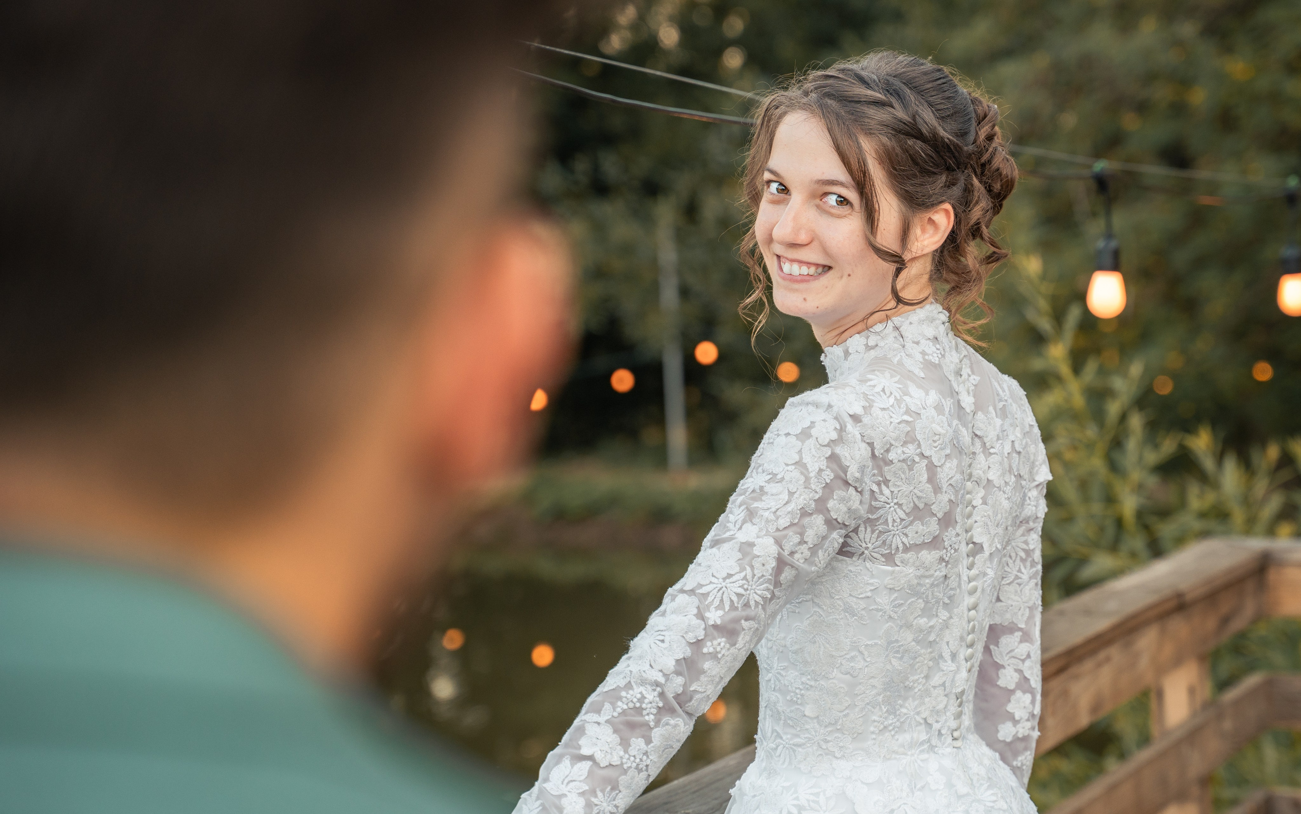 Mireasă zâmbind peste umăr către cameră, ghirlande de lumini în fundal, nuntă în aer liber seara, incadru.ro.