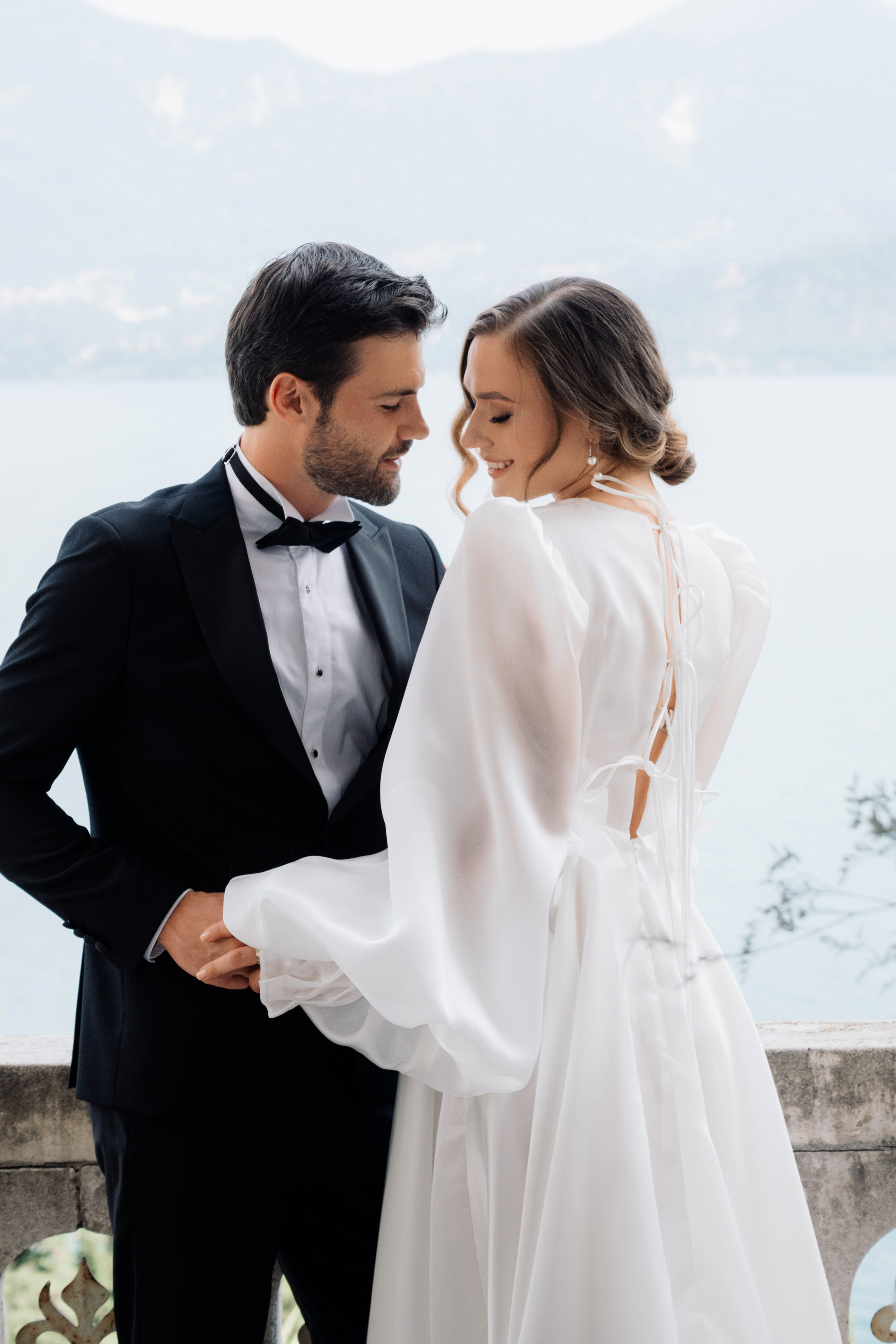 a bride and groom standing on a balcony overlooking the lake