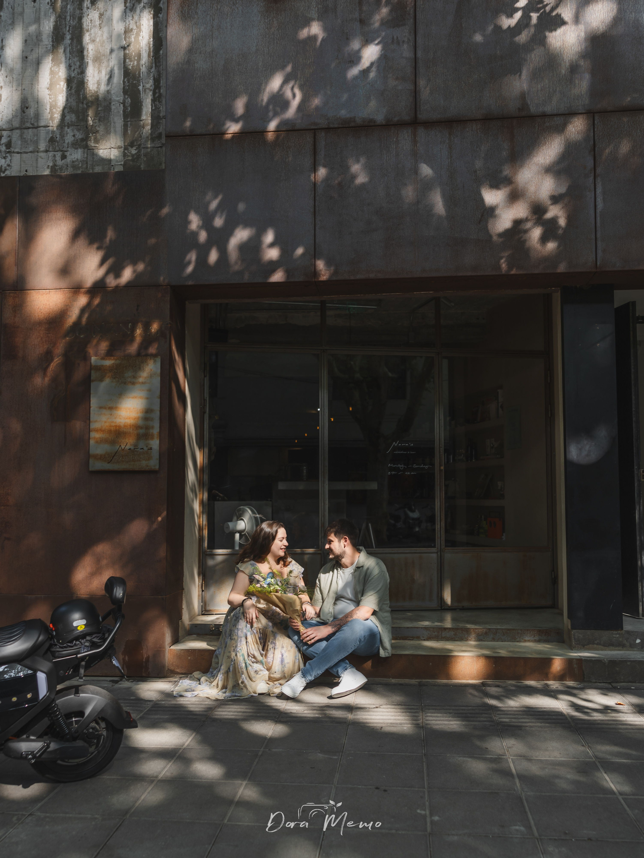A wide environmental portrait of an expecting couple sitting outside a cafe during their Shanghai maternity session.