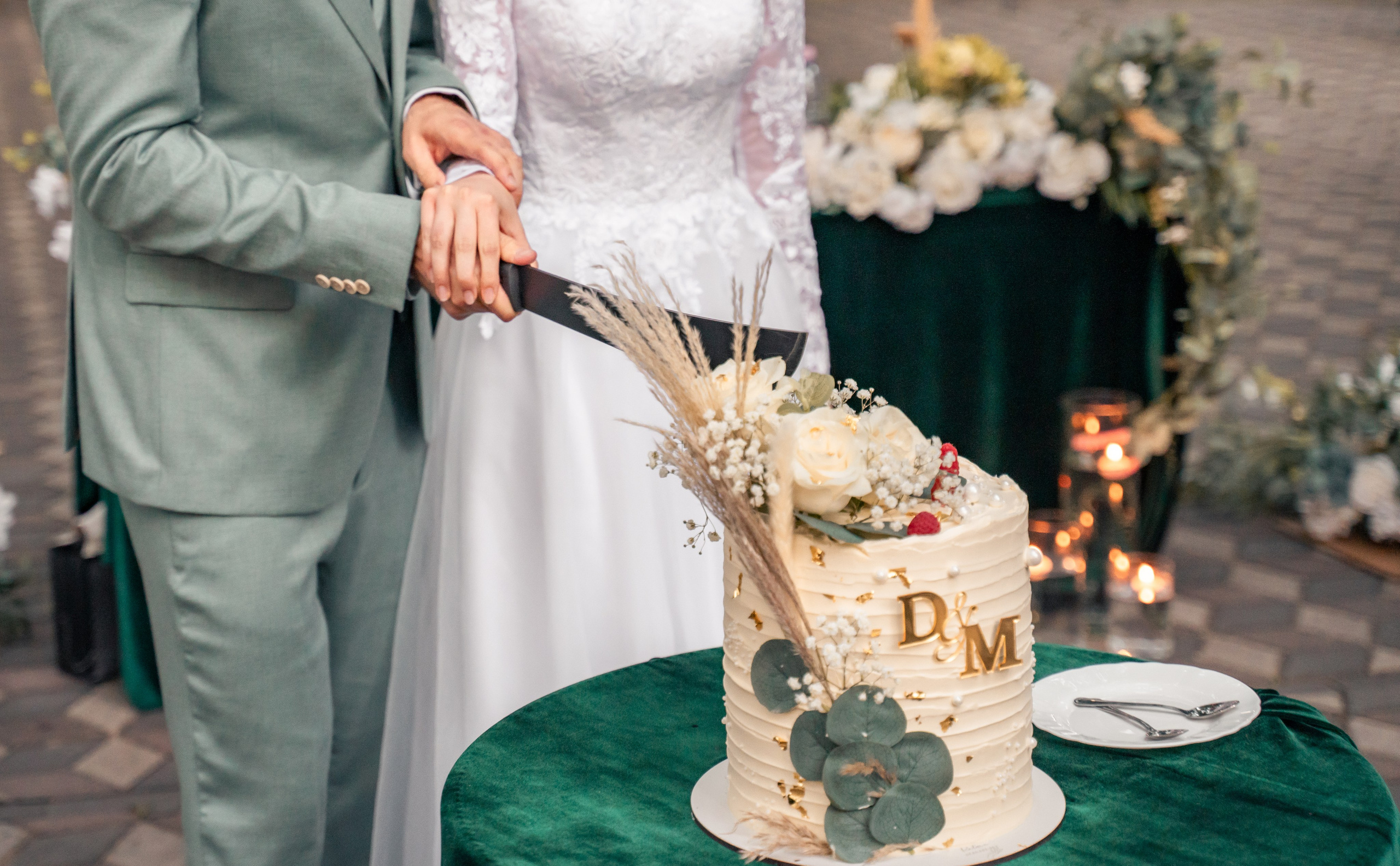 Miri tăind tortul de nuntă alb cu inițiale aurii D&M, decor cu flori albe și eucalipt, incadru.ro.