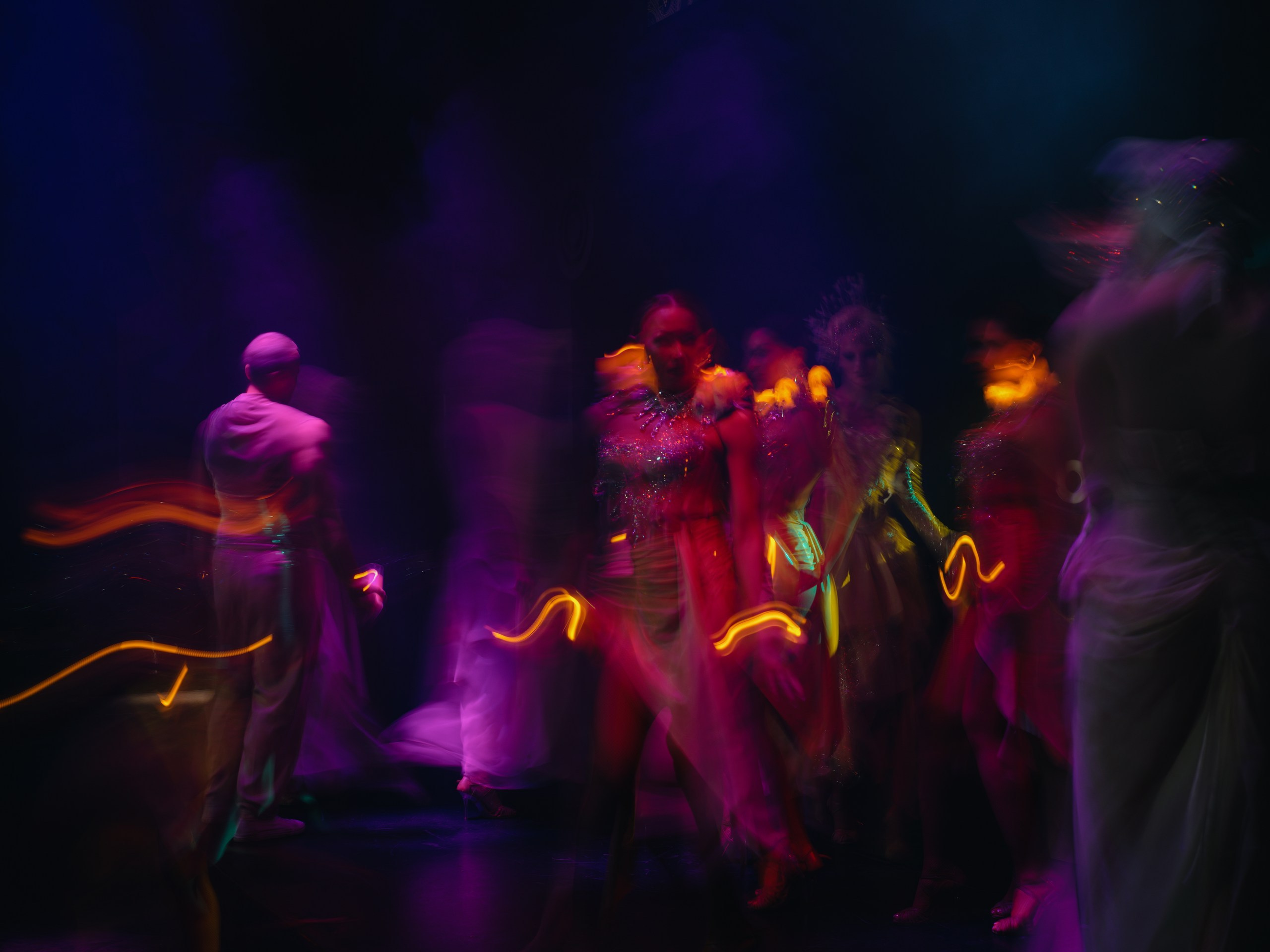 Silhouettes of dancers against massive LED screens and laser beams.