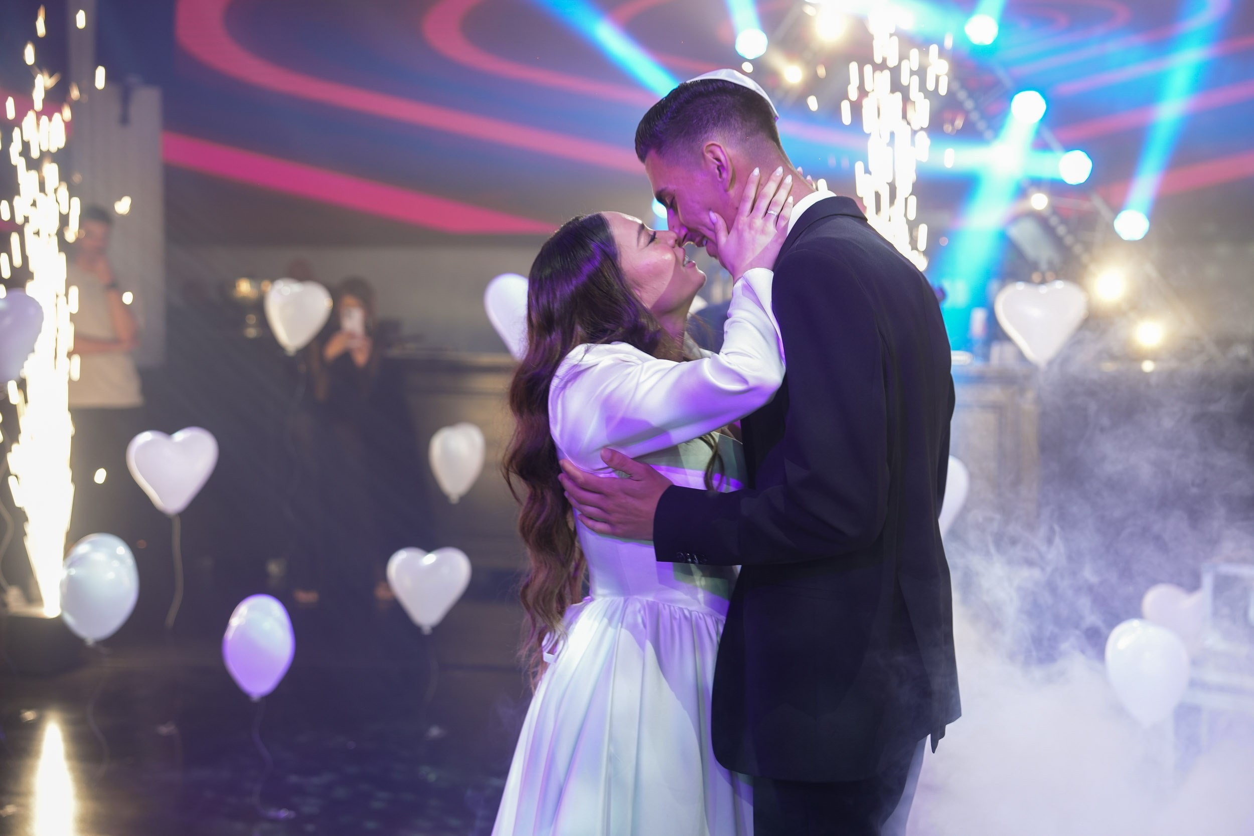 A bride and groom dance surrounded by low-lying smoke, sparklers, and heart-shaped balloons