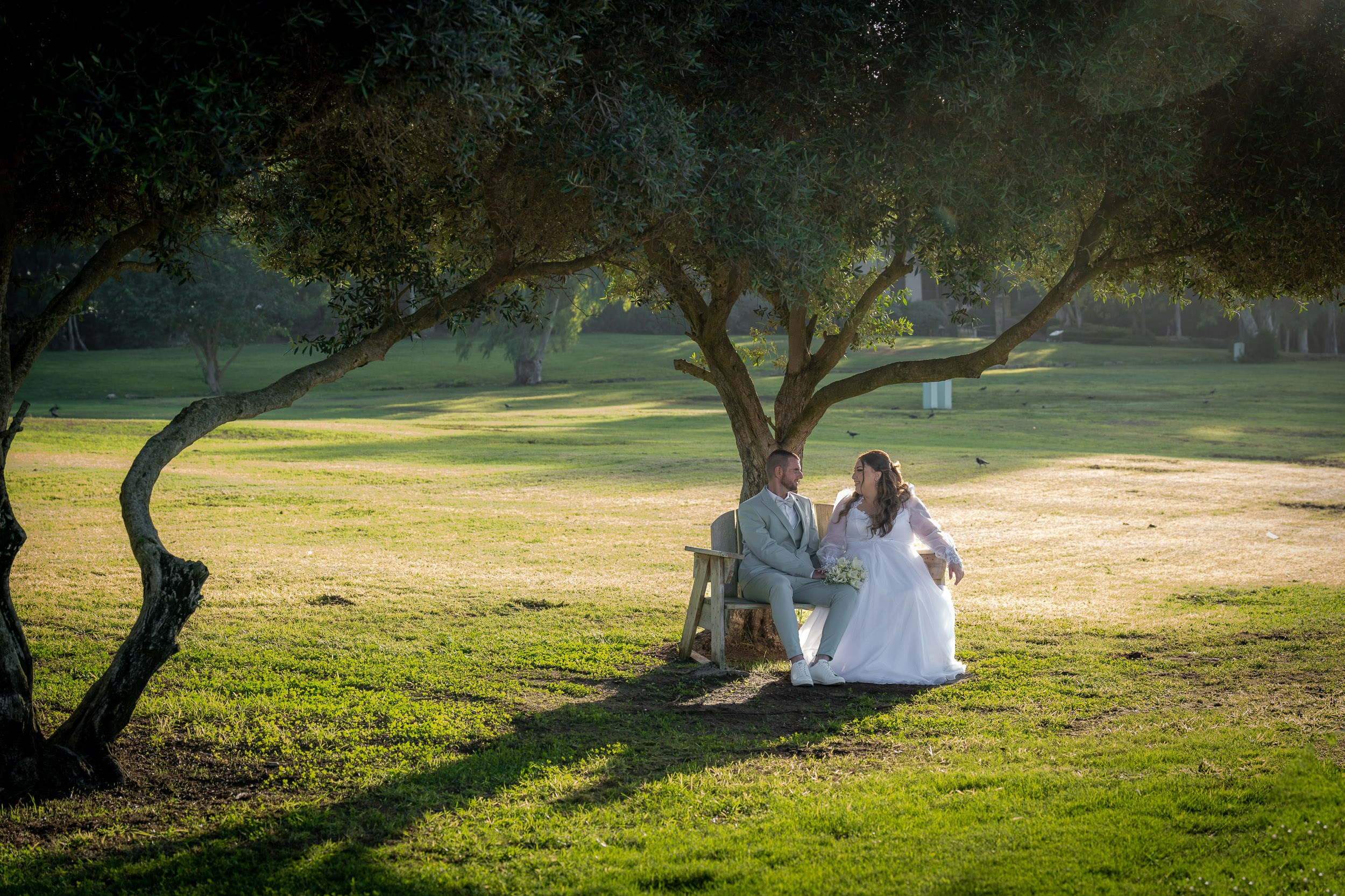 Ella and Matan sit together beneath a large tree