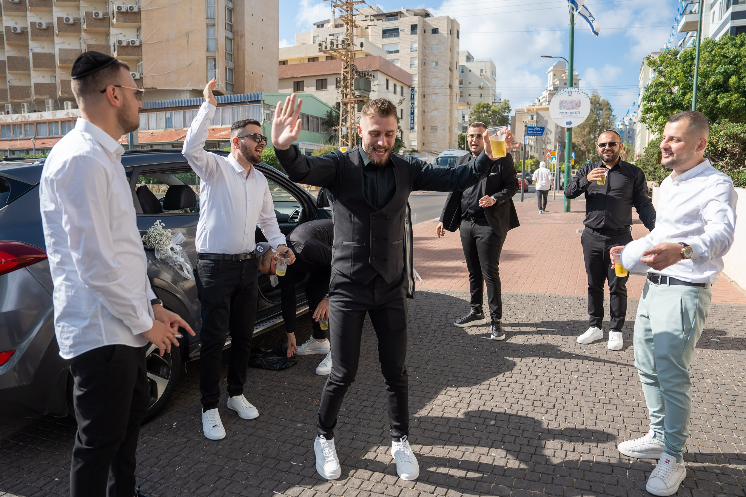 Groomsmen and wedding guests drinking beer and dancing by a decorated car in Netanya, Israel