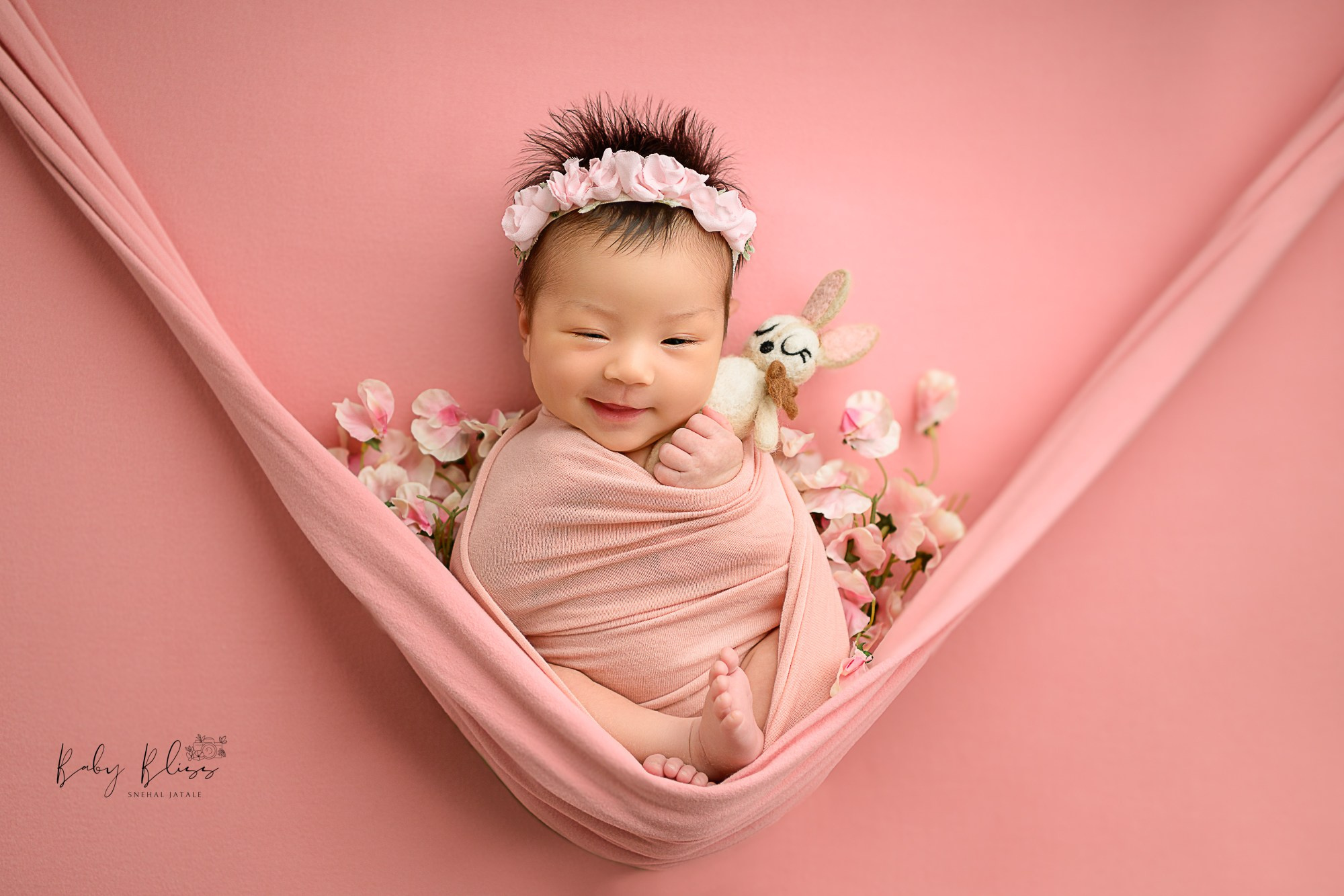smiling newborn baby girl in light pink wrap and floral setup 