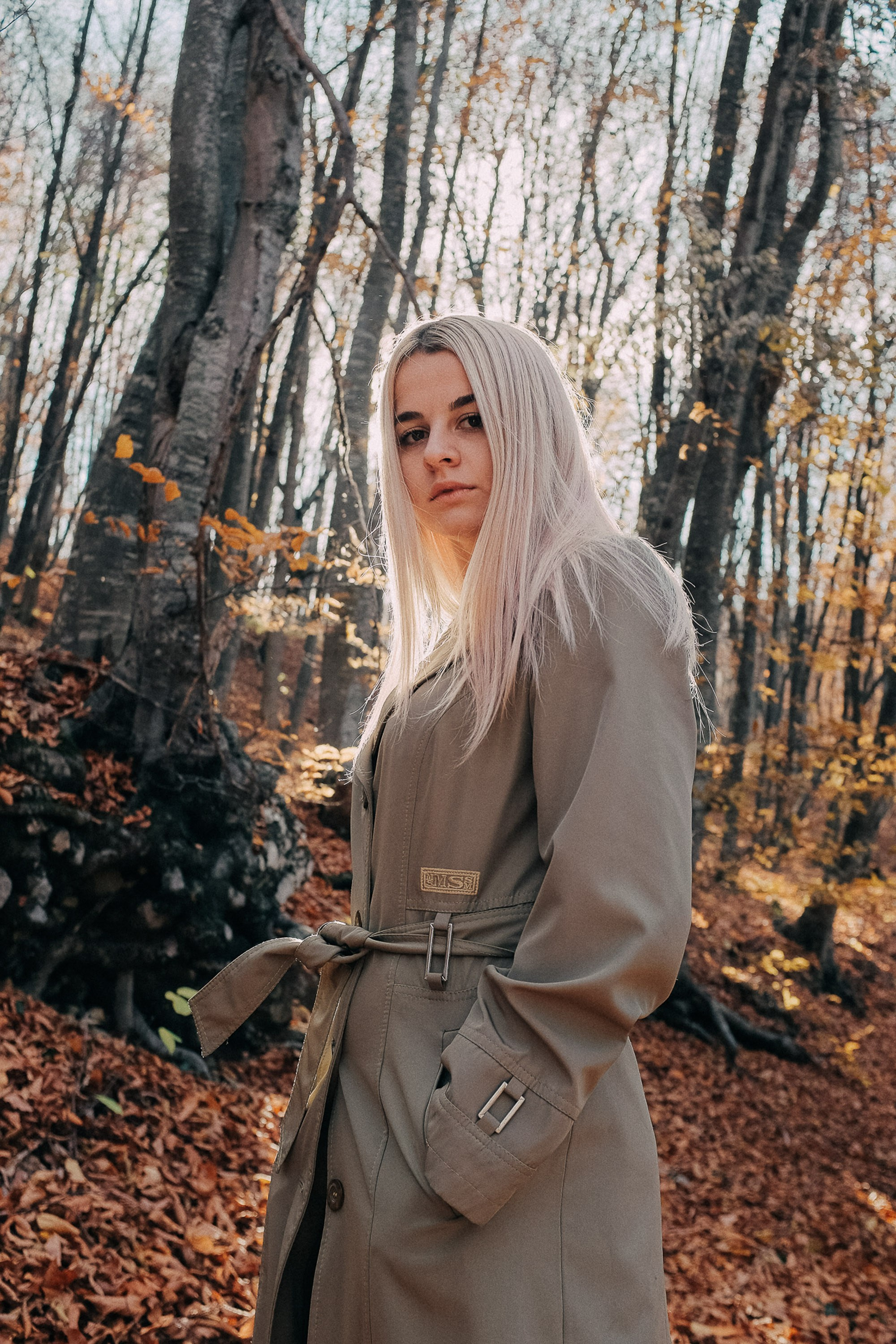 Blonde woman in beige coat among birch trees