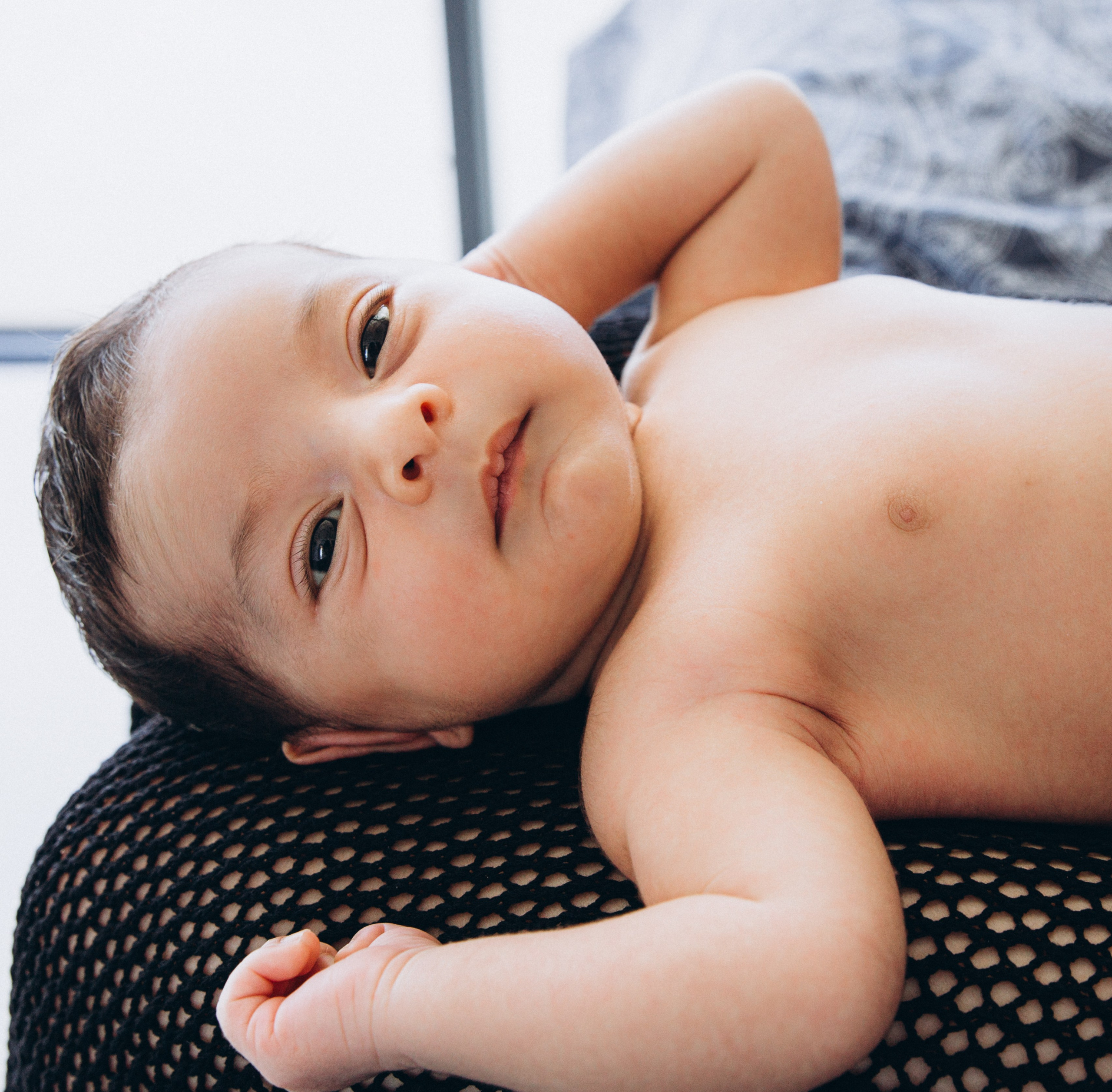 Retrato íntimo de recién nacido en Alicante, España — imagen tierna de un bebé tumbado con ojos curiosos y luz natural suave. Ideal para familias que buscan sesiones de recién nacido en Alicante y la Costa Blanca.