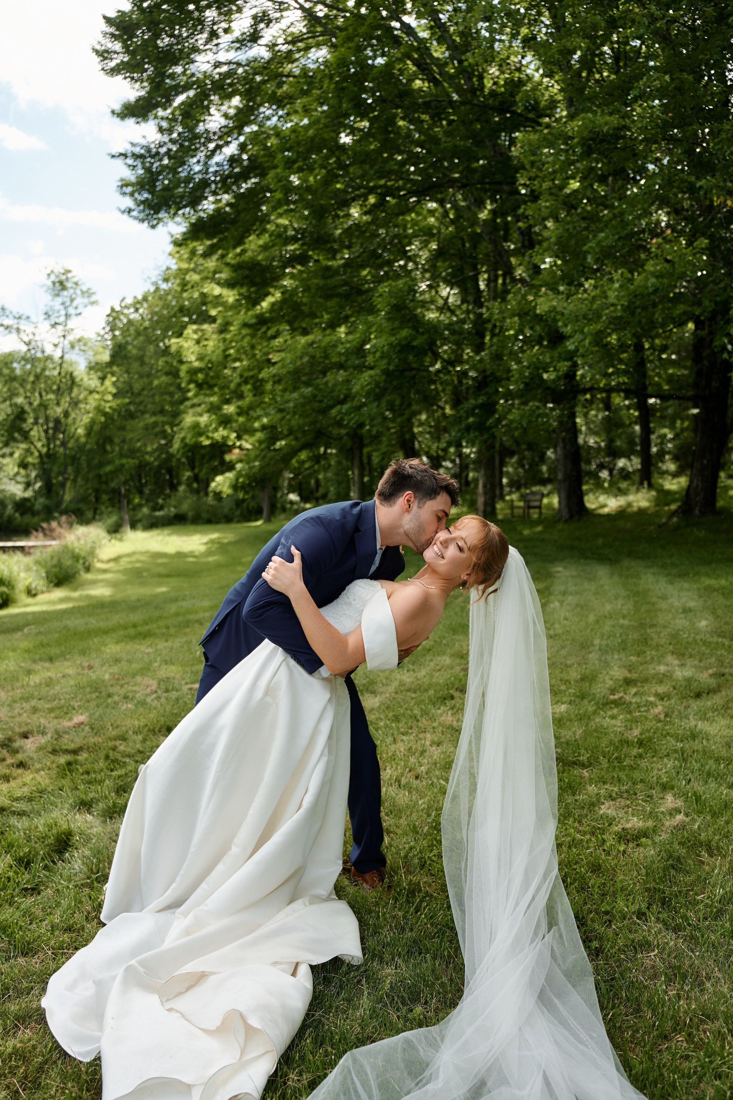 Outdoor wedding photography of groom kissing bride in lush green park in New Jersey