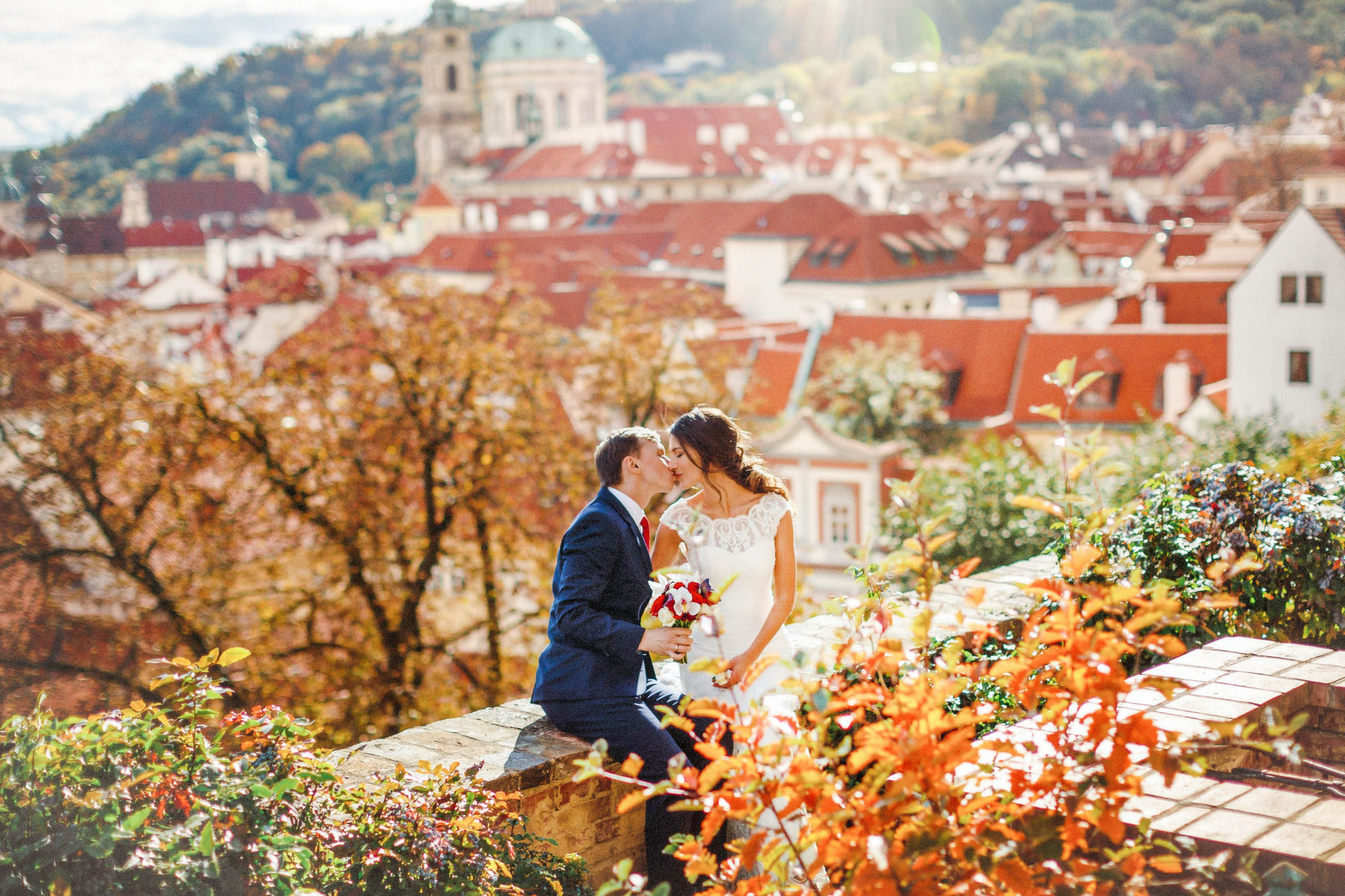 Couple lovingly kiss in a garden setting above Prague surrounded by the rich colors of autumn.