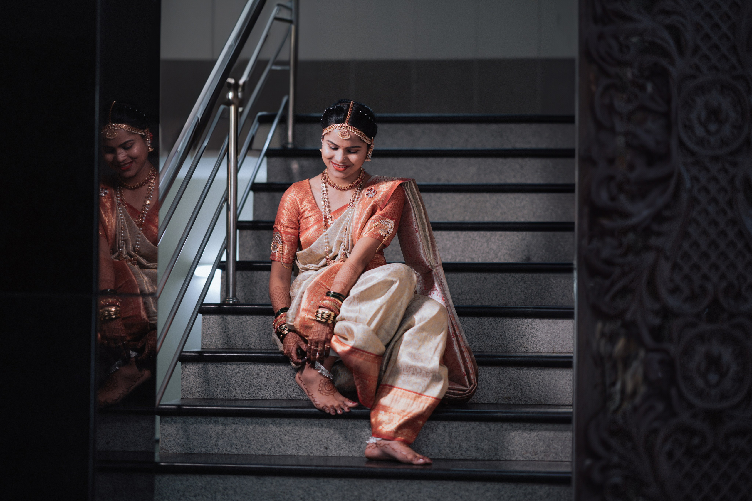 candid indoor photo of a smiling South Indian bride sitting on a modern staircase in a wedding hall in Malleshwaram, Bengaluru
